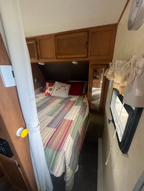 An inviting RV rental bedroom with a colorful quilt, overhead cabinets, and a compact design, perfect for travel.. Coachmen Apex 2013