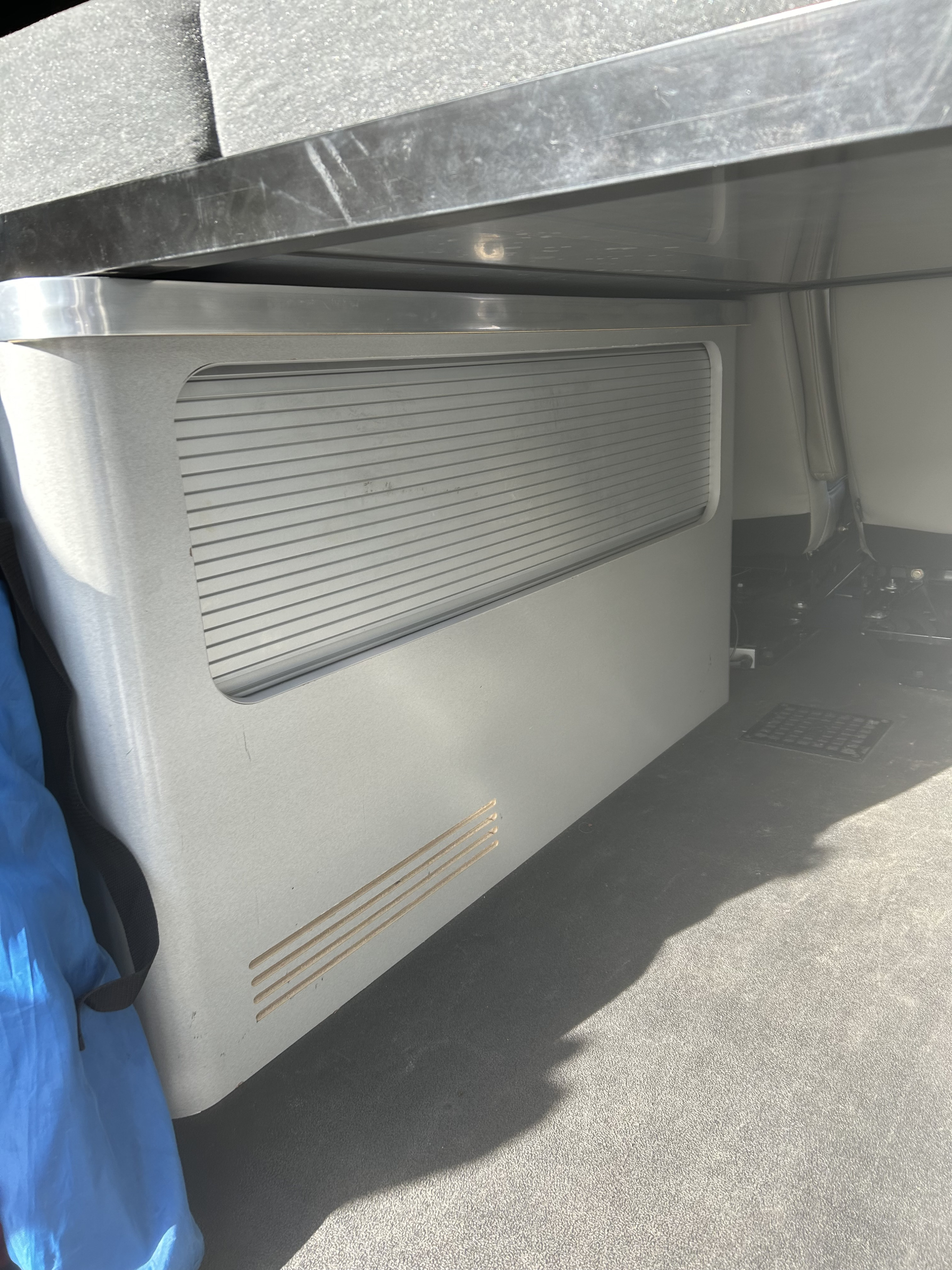 An RV rental interior reveals a silver built-in unit with horizontal vents, under a dark surface, on a grey floor.. Modvan CV1 Ford Transit 2021
