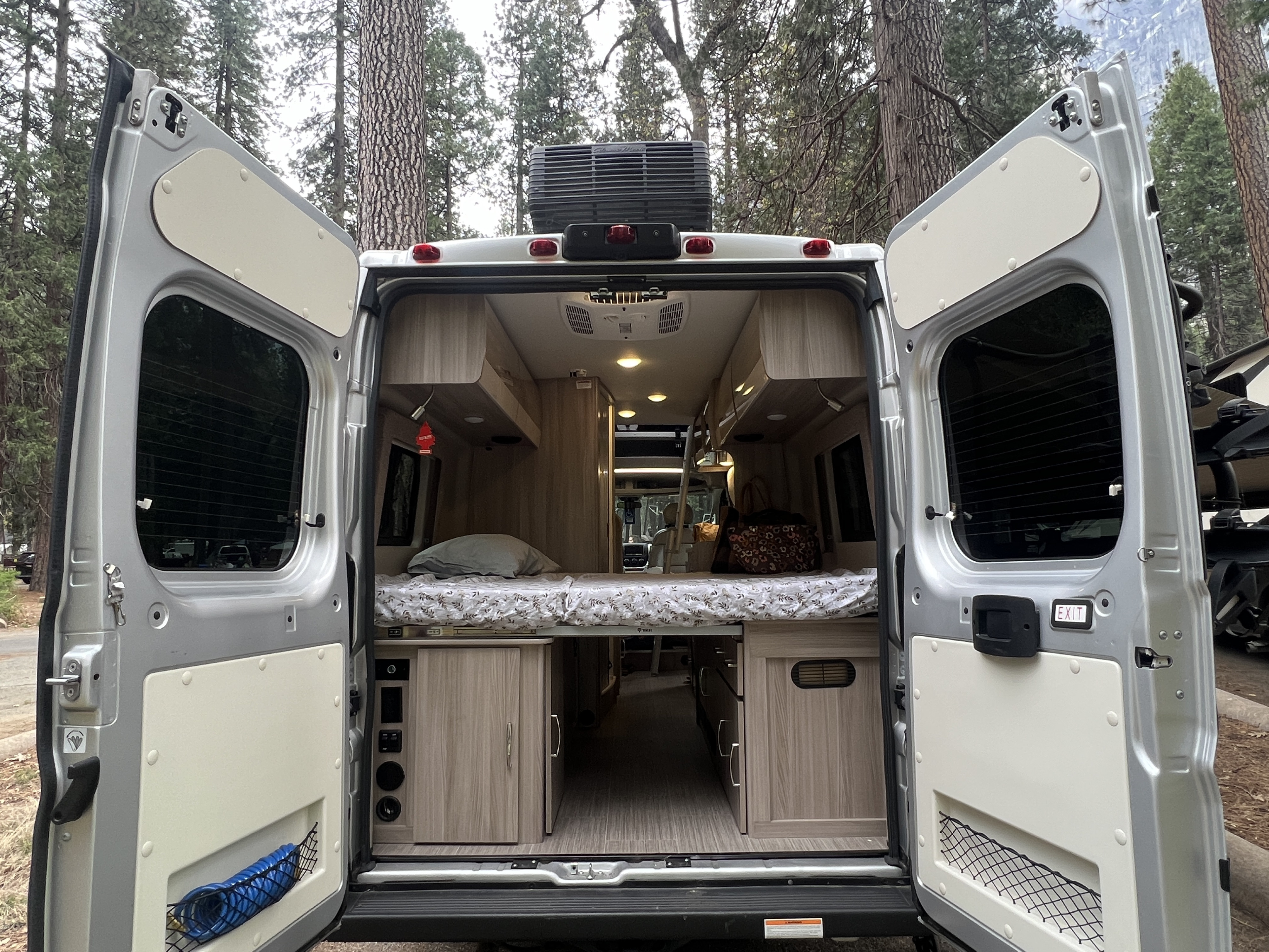 Rear view of an RV rental camper van, doors open to reveal a comfortable bed, light wood cabinetry, and integrated controls.. Thor Motor Coach Sequence 2022