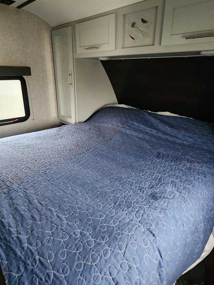 Cozy RV rental bedroom with a large bed, blue quilt, white cabinets, and a window, perfect for comfortable travel.. Keystone RV Bullet Ultra Lite 2020