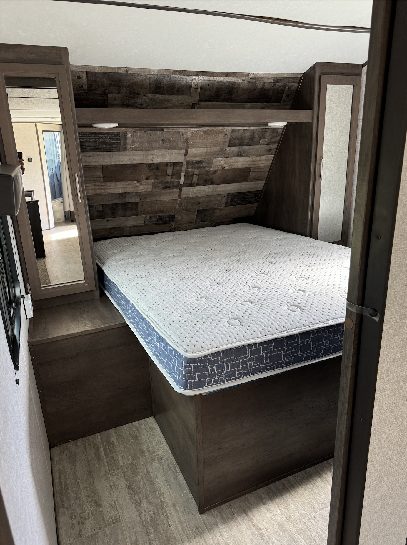 Cozy RV rental bedroom: a comfy bed with white mattress, dark wood headboard, and built-in storage with a mirror.. Aspen Trail Aspen Trail Trailer 2021