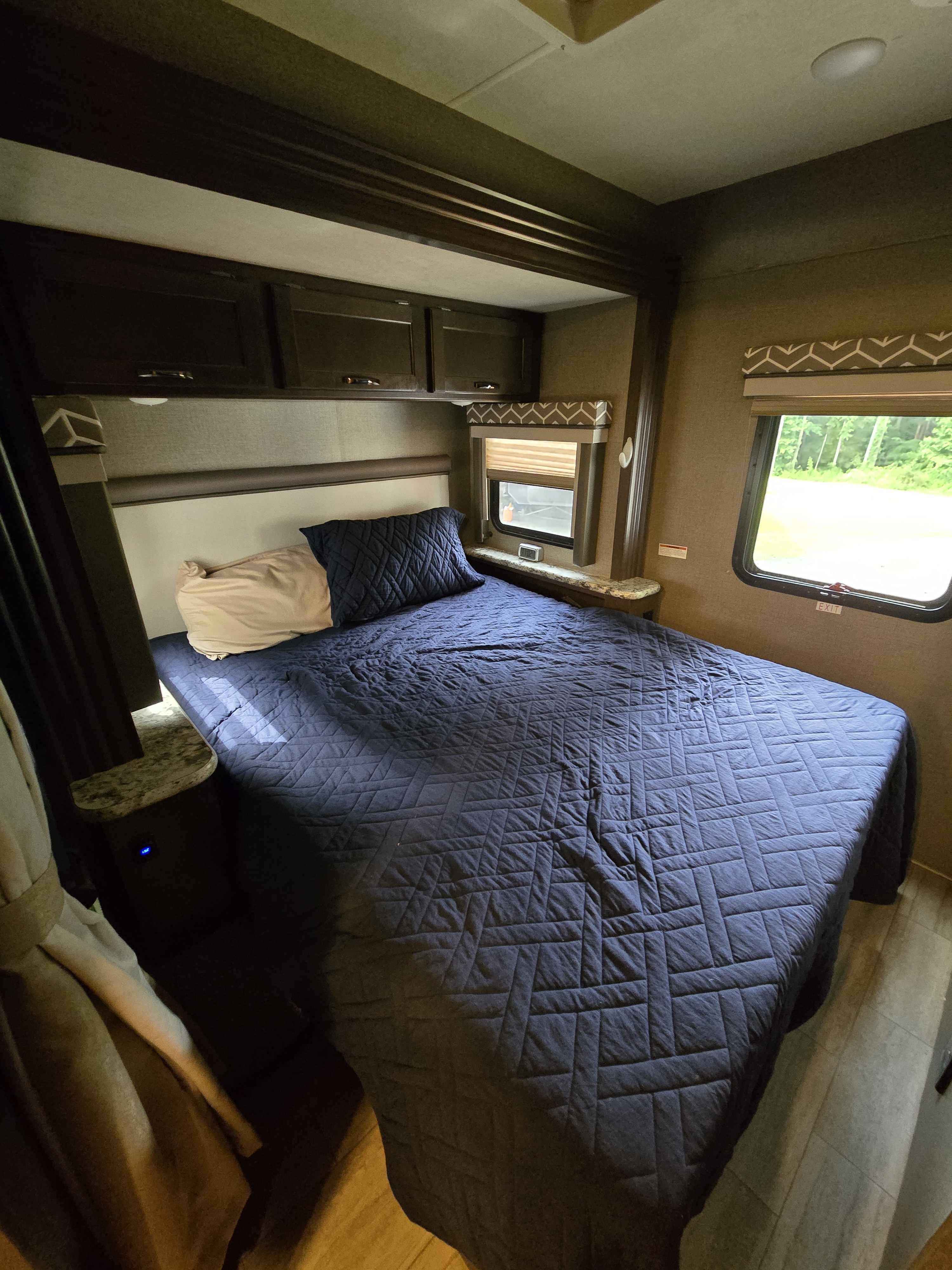 Cozy RV rental bedroom featuring a bed with dark blue quilt, built-in cabinets, and a window with an outdoor view.. Thor Freedom Traveler 2020