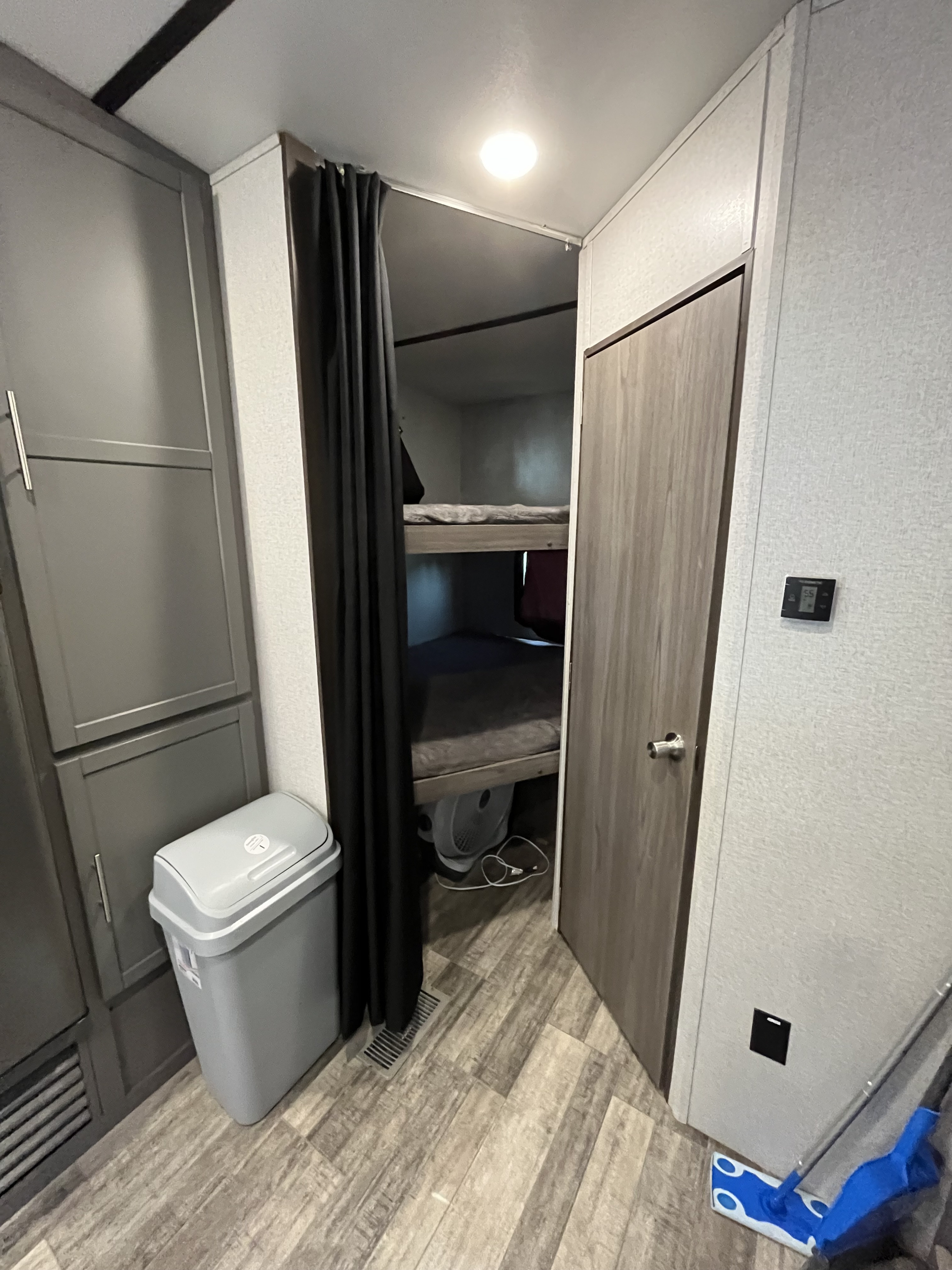 RV rental interior: bunk beds with a privacy curtain, grey storage cabinets, and wood-look flooring.. Keystone RV 270BH 2022
