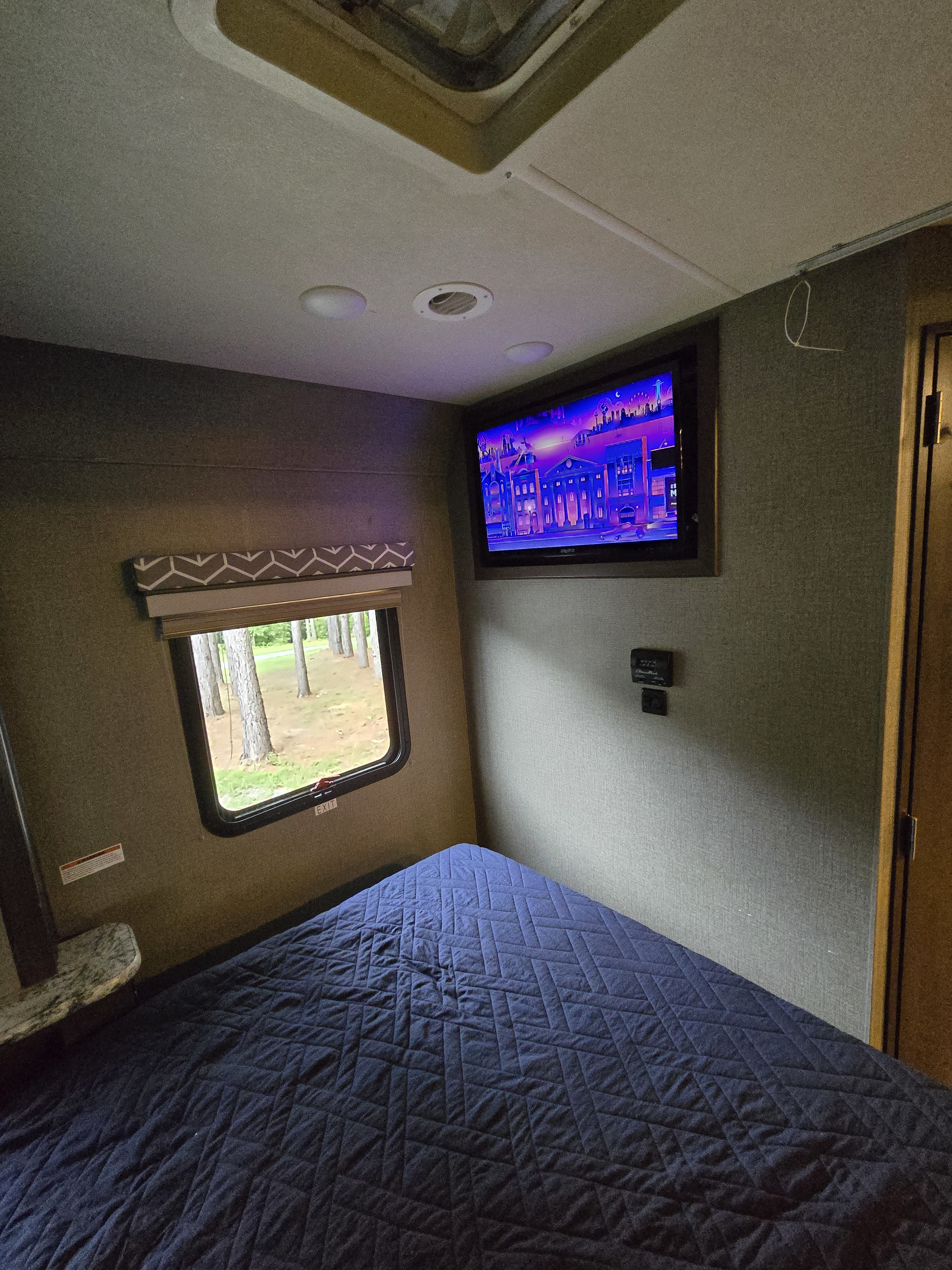 Inside a comfy RV rental bedroom. Features include a quilted bed, TV, window view, and climate controls.. Thor Freedom Traveler 2020