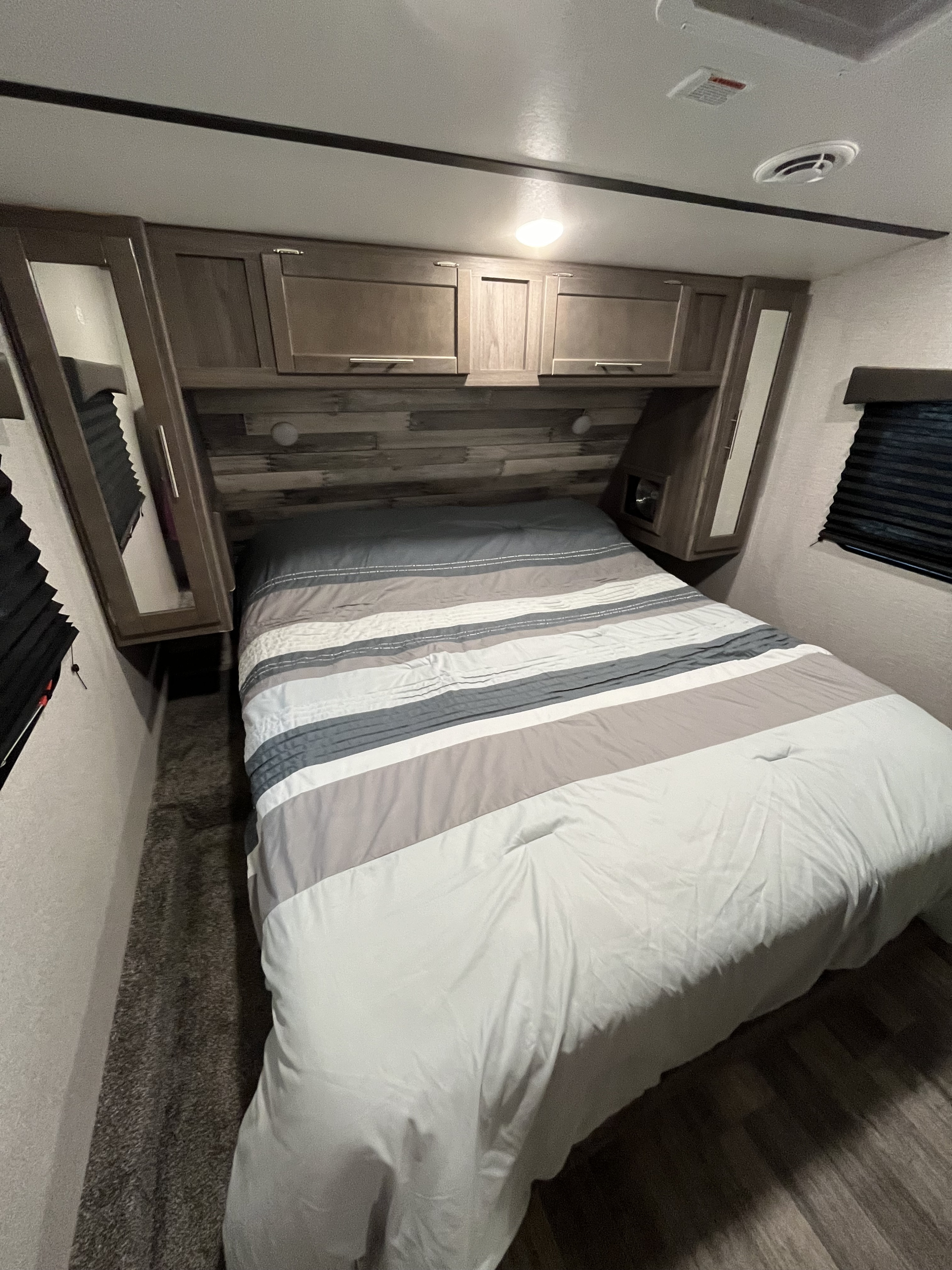 Comfortable RV rental bedroom featuring a striped bed, overhead storage, and dual window blinds in a compact interior.. Keystone RV 270BH 2022