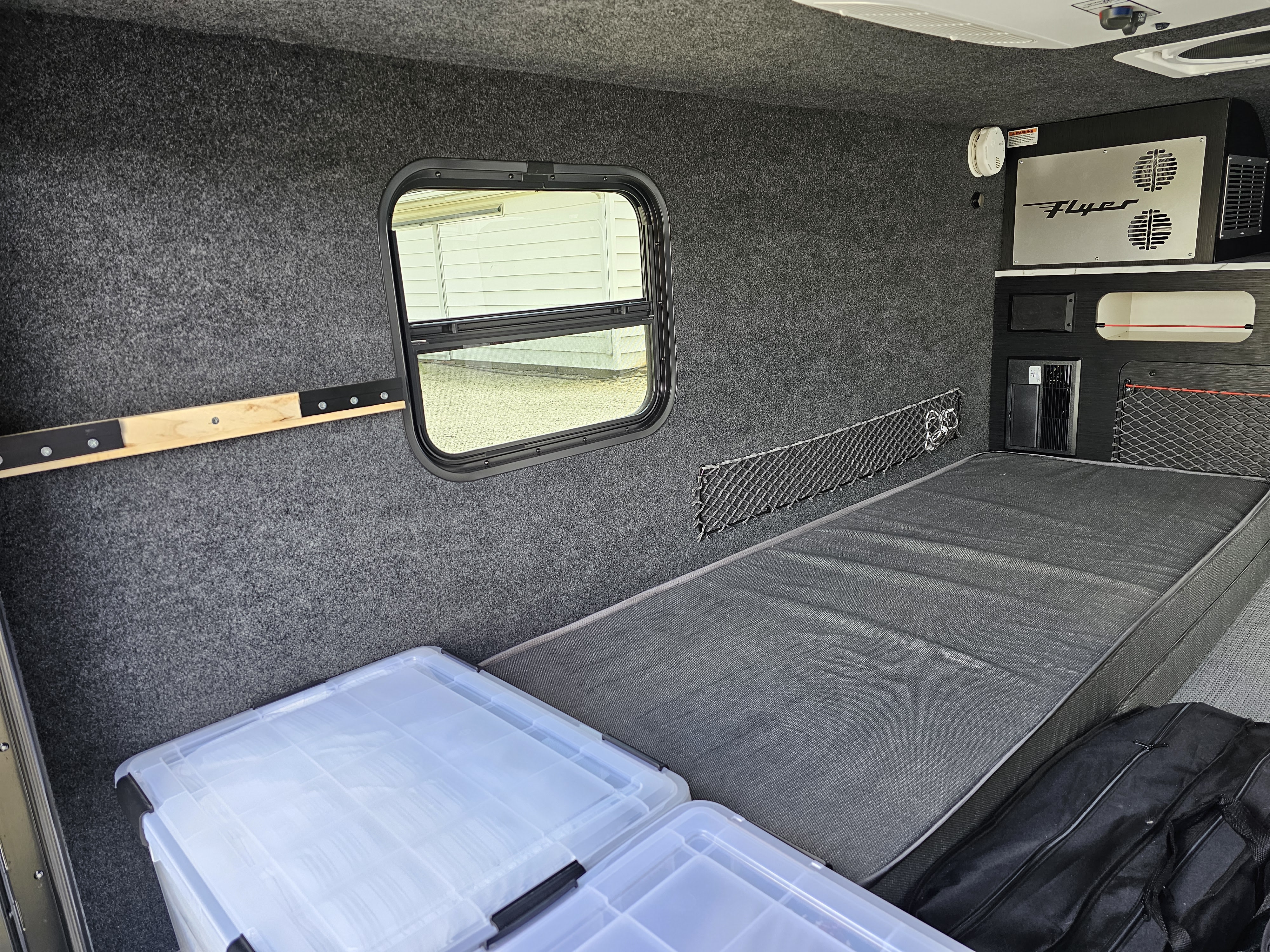 Inside this RV rental, find a cozy bed, window, and built-in storage within grey carpeted walls, an organized camper interior.. InTech RV Flyer 2024