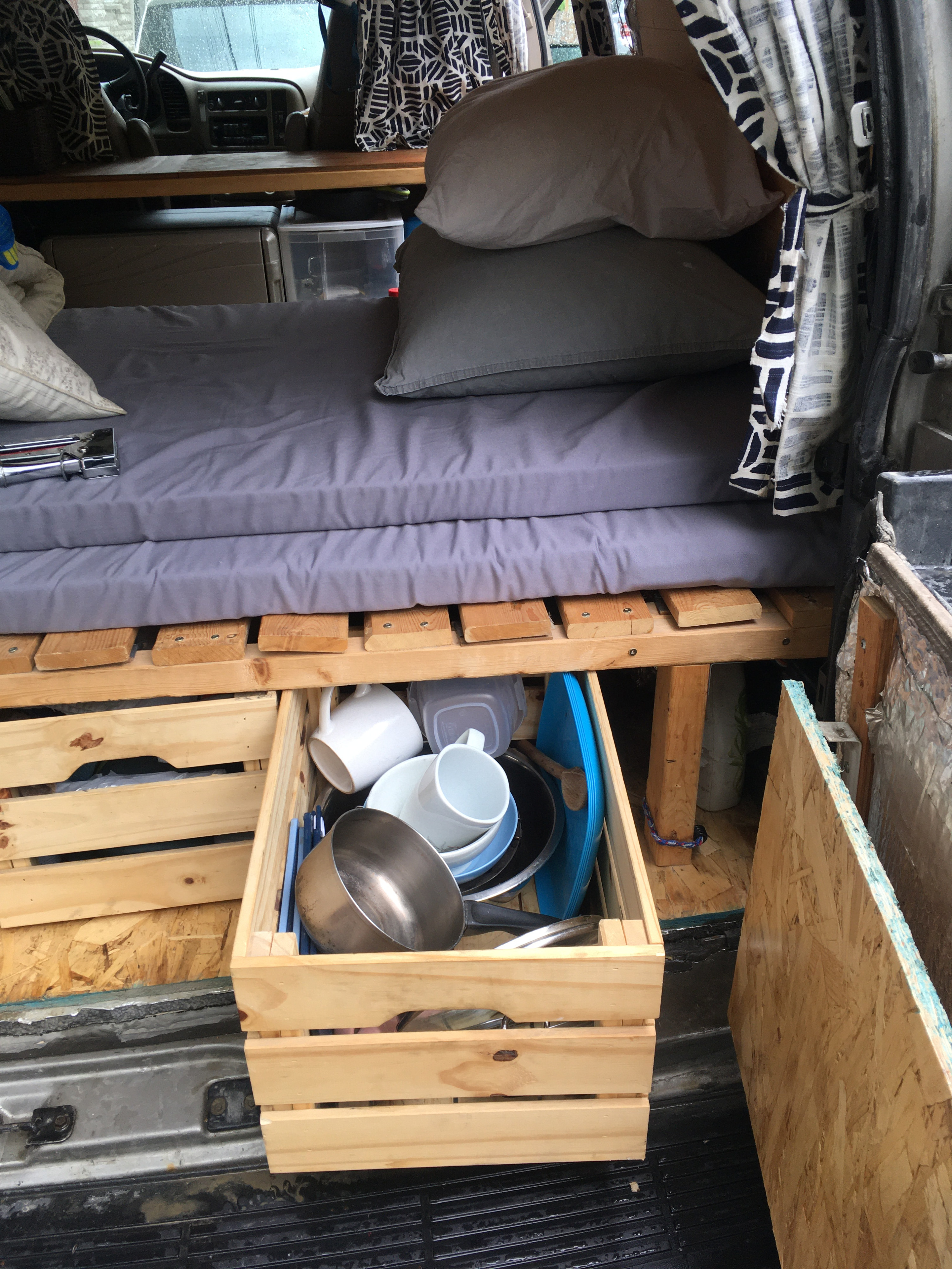 RV rental camper interior features a bed on wooden pallets and under-bed storage crates with kitchenware.. GMC Safari 2002