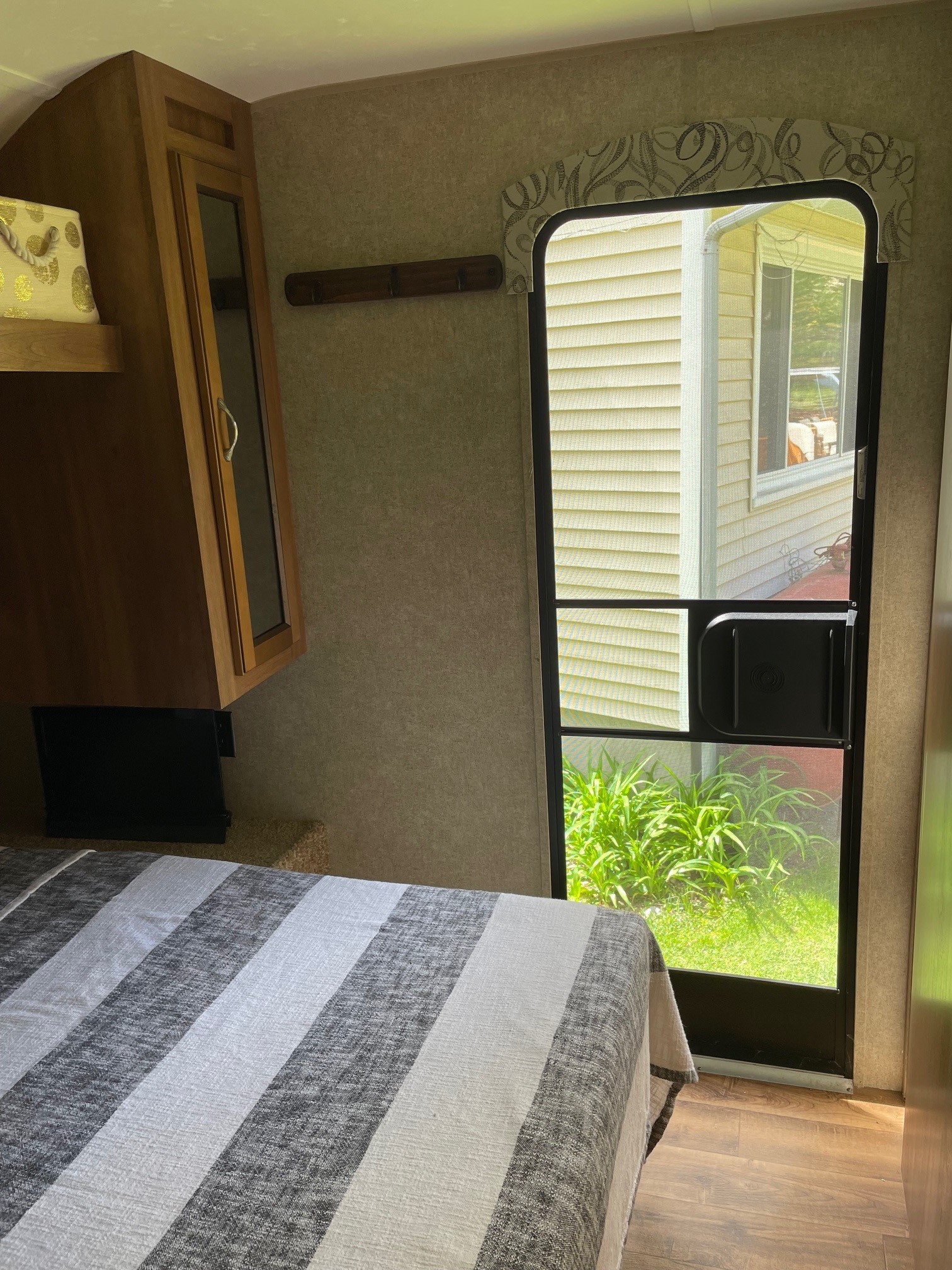 Inside a cozy RV rental bedroom: striped bed, wood cabinets, and screen door opening to a lush outdoor view.. Forest River Coachmen Catalina 2016