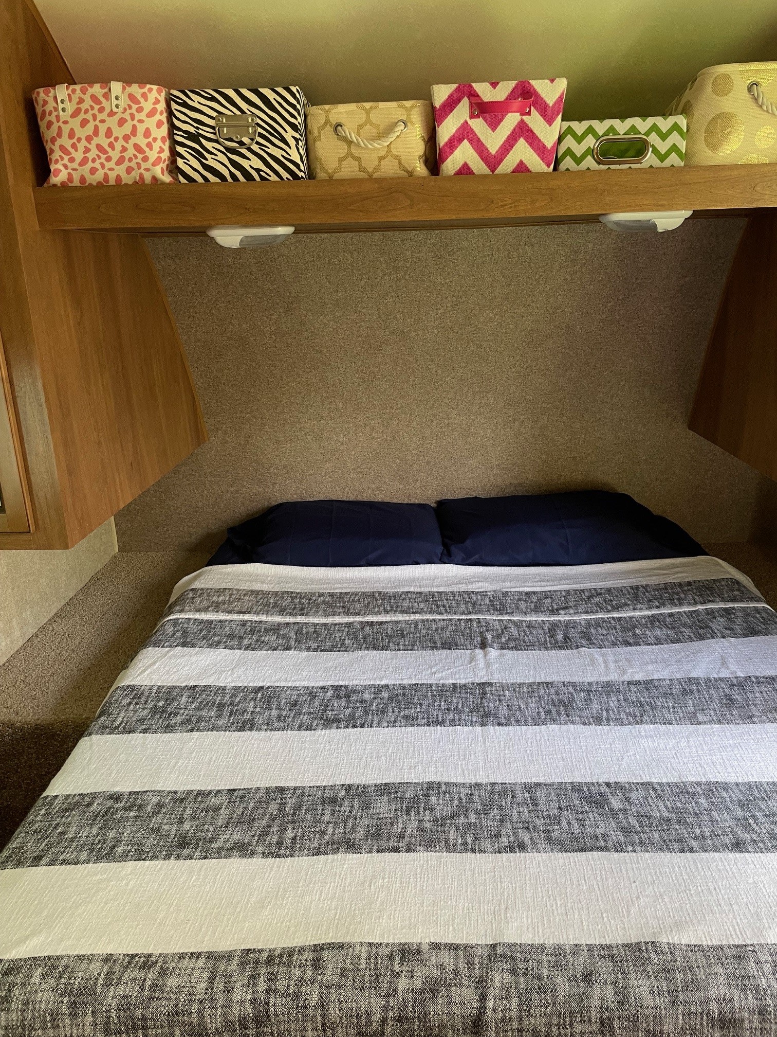 Cozy RV rental bedroom features a striped bed, navy pillows, & patterned storage bins on a shelf for organized living.. Forest River Coachmen Catalina 2016