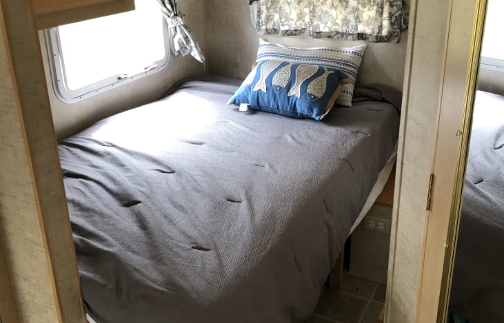 Cozy RV rental bedroom features a gray bed, blue fish-patterned pillow, and bright window with curtains.. Jayco Jay Feather EXP 2005