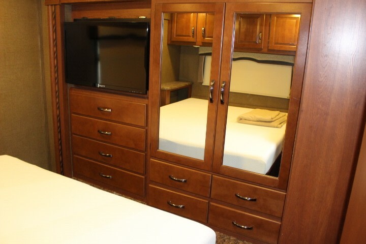 RV rental bedroom showing a built-in unit with TV, dresser drawers, and mirrored wardrobe doors reflecting the bed.. Thor Chateau 2016