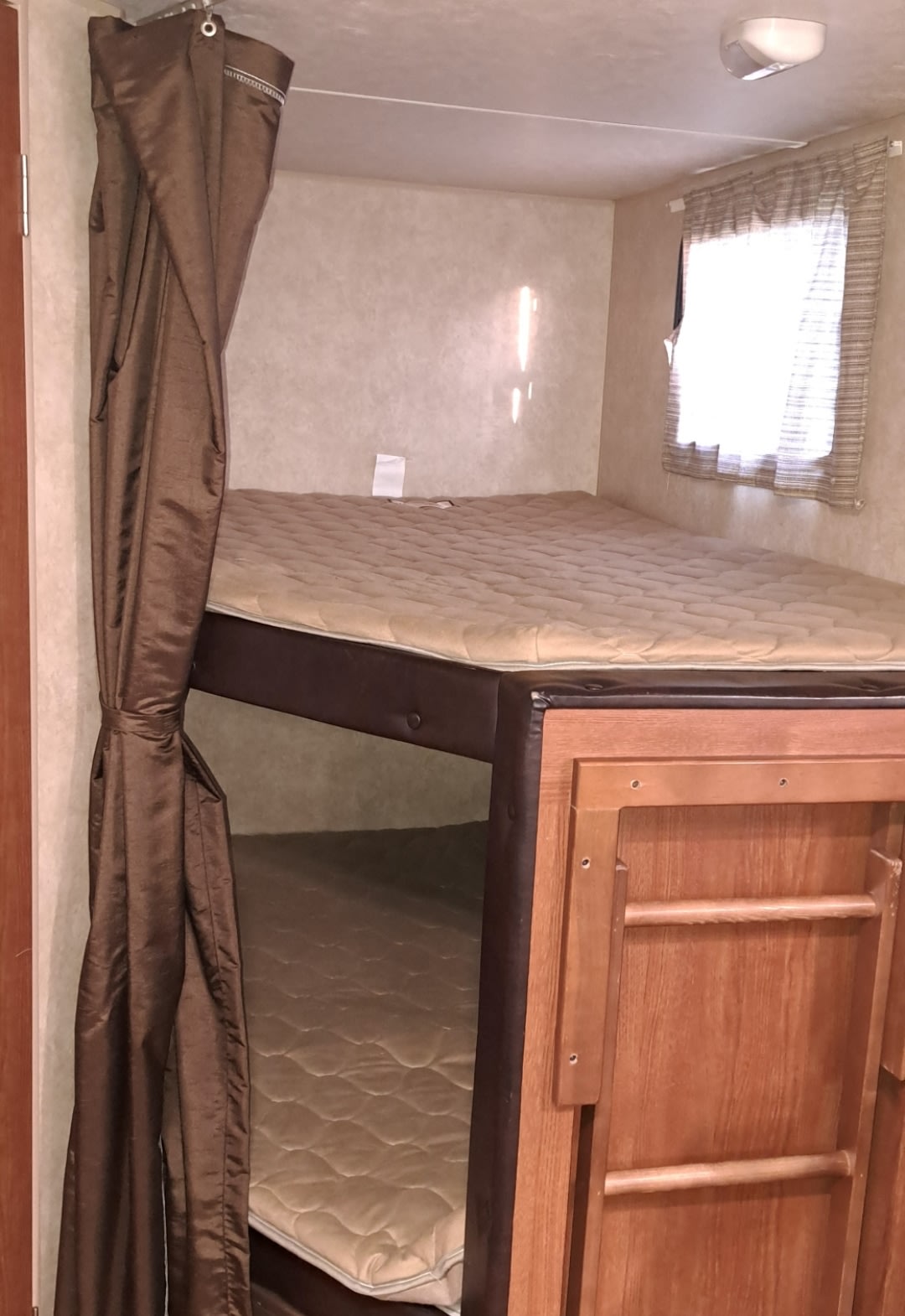 RV rental bunk beds: cozy sleeping area with mattresses, brown privacy curtains, and a window, ideal for family travel.. Forest River Wildwood X-Lite 2015