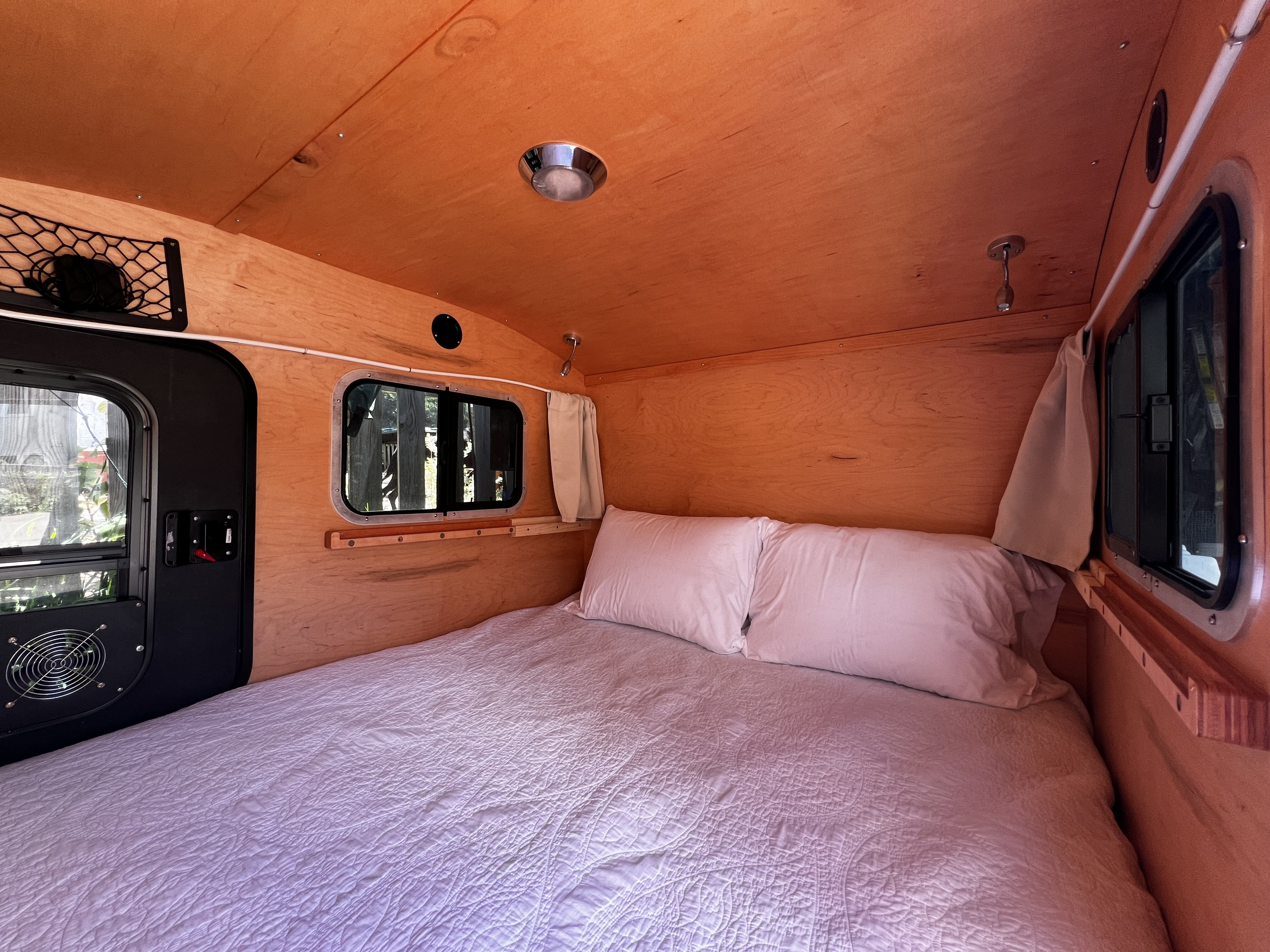 Explore a compact RV rental interior with a comfy bed, wooden accents, and functional windows for cozy mobile sleeping.. TC Teardrop 5x10 Overland 2021