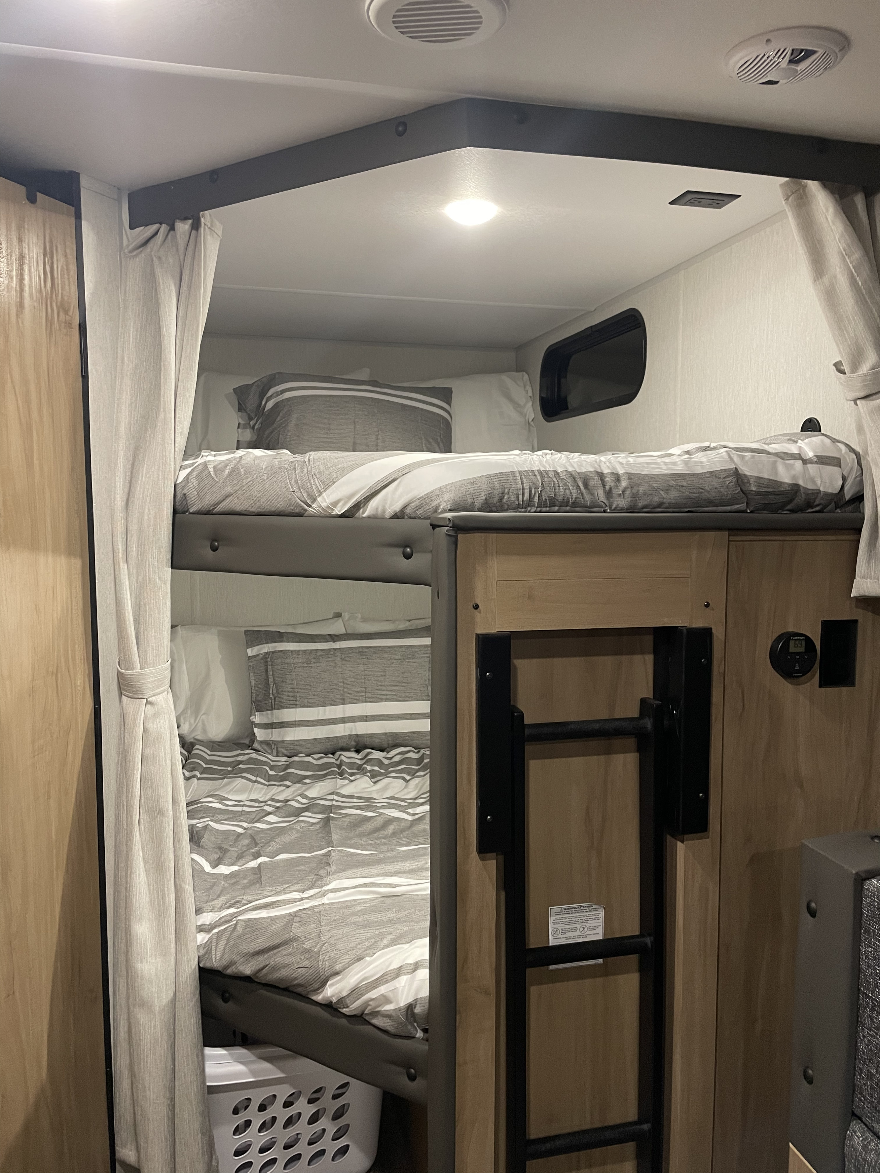 RV rental interior showing cozy bunk beds with striped bedding, a ladder, and a control panel for comfort.. Forest River Cherokee Grey Wolf 26BDH 2024