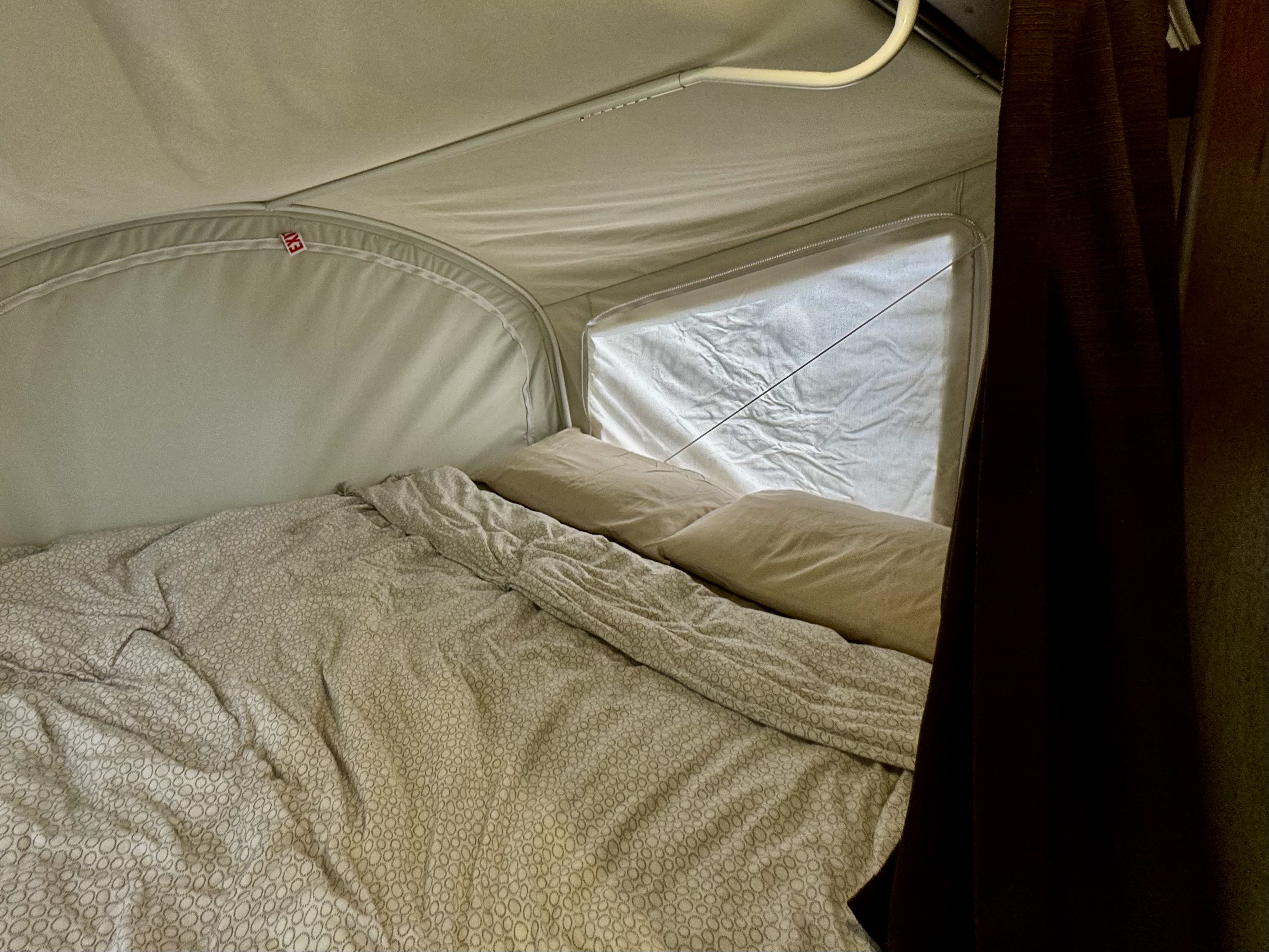 Cozy sleeping area inside an RV rental pop-up camper, featuring a bed with patterned bedding, pillows, and a window.. Jayco Jay Feather X17Z 2019