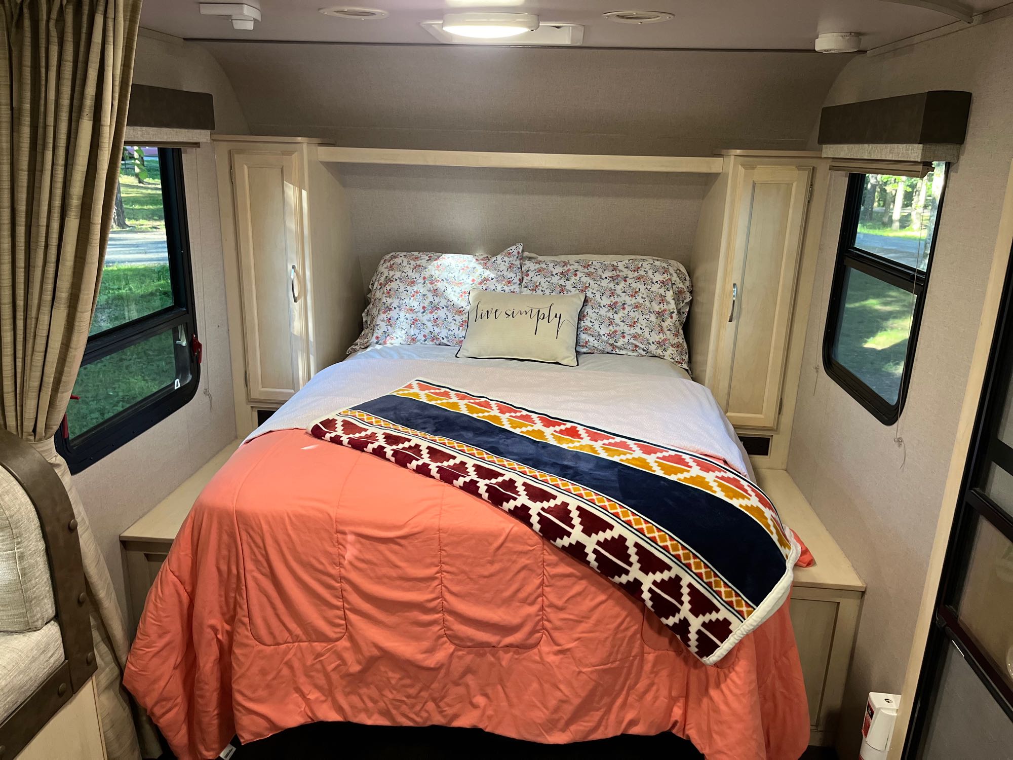 Cozy RV rental bedroom features a bed with coral bedding, floral pillows, and a patterned throw, ready for your travels.. Winnebago Micro Mini- 2108DS 2020
