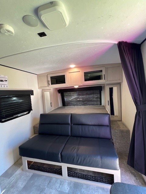 RV rental interior: A compact space with a comfortable sofa, raised bed, and overhead cabinets for storage.. Coachmen Apex Nano 2022