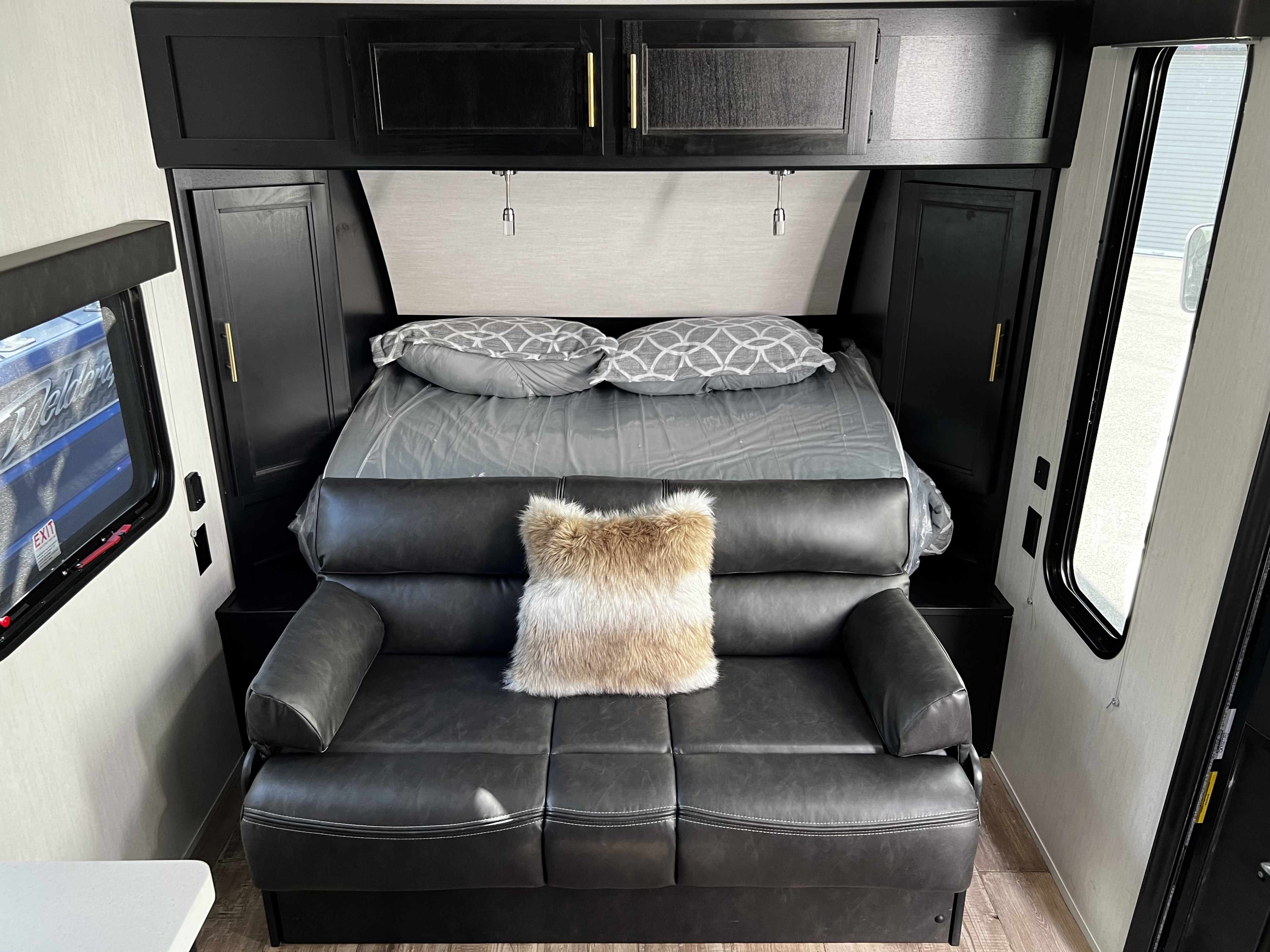 RV rental interior featuring a compact bedroom & living space: bed with plastic cover, overhead storage, and a sofa.. Forest River Cherokee Wolf Pup 2023