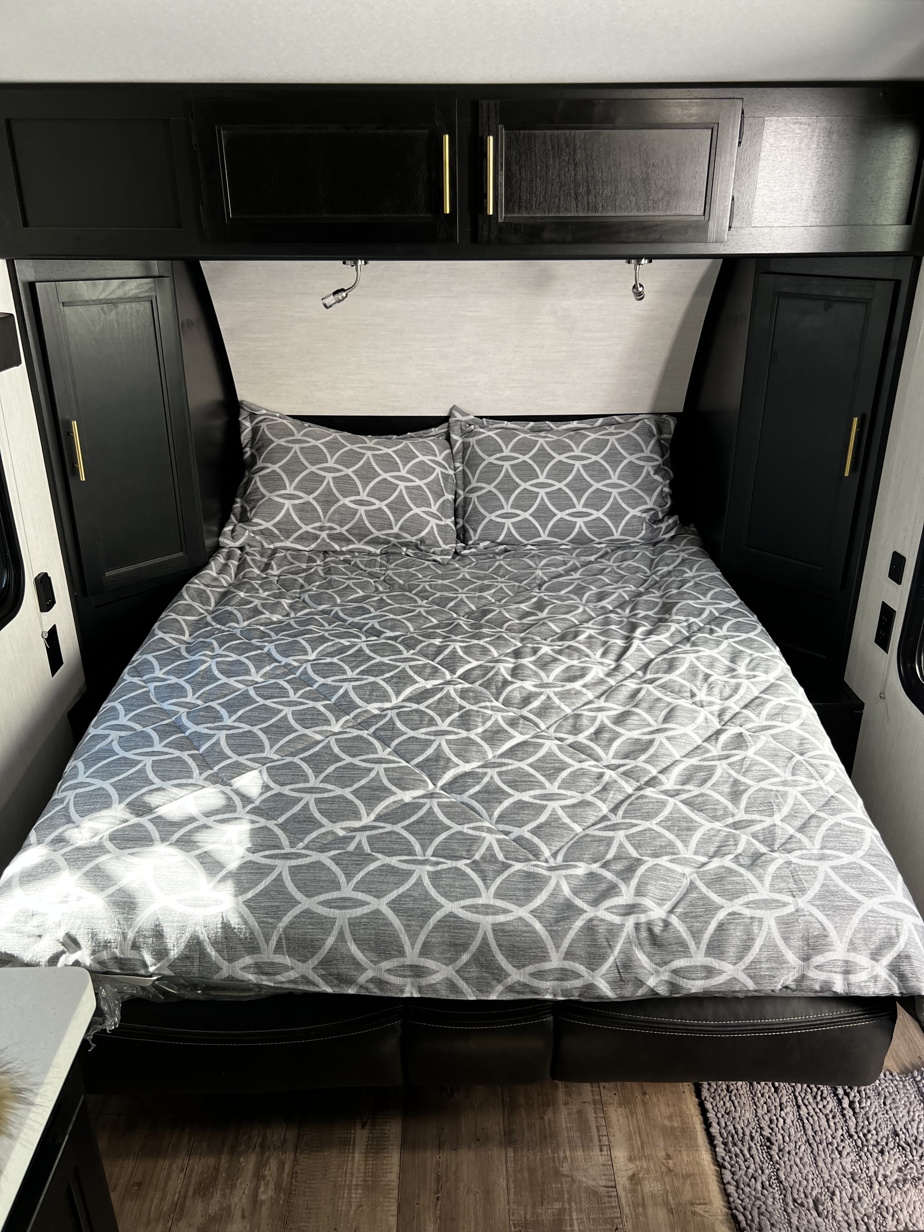 RV rental bedroom with a comfy queen bed featuring modern grey geometric bedding. Dark overhead and side cabinets offer ample storage.. Forest River Cherokee Wolf Pup 2023