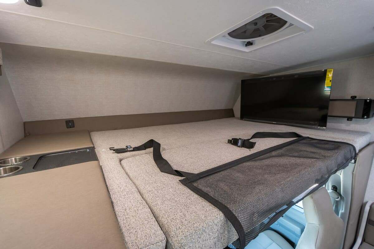 RV rental's overhead bunk features a bed, TV, ceiling vent, safety net, and cupholders for comfort.. Forest River Coachmen Freelander 2025