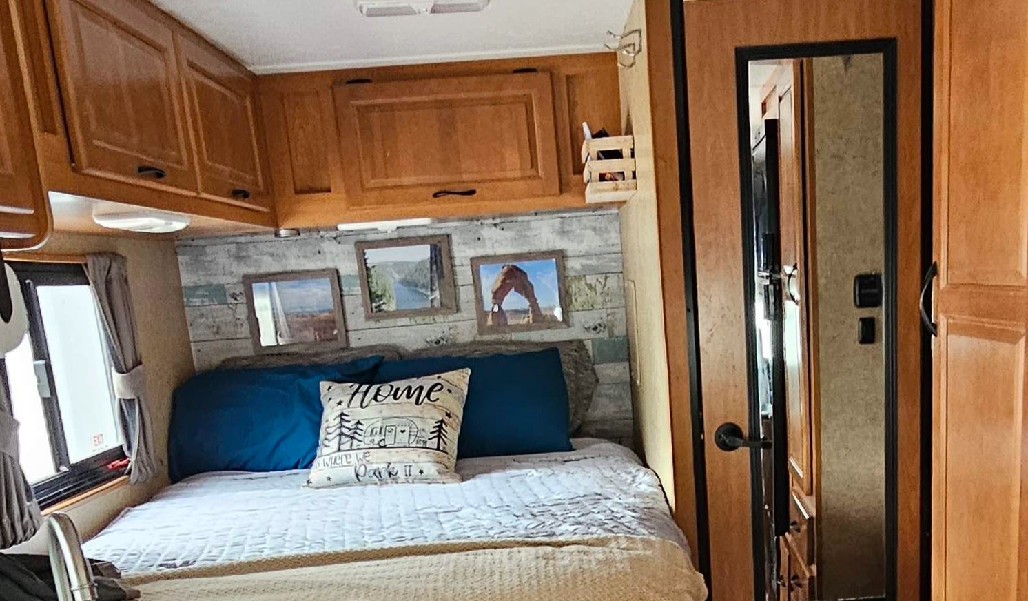 This RV rental interior features a cozy bedroom with rustic wood paneling, overhead cabinets, and framed travel art.. Thor Majestic 2013
