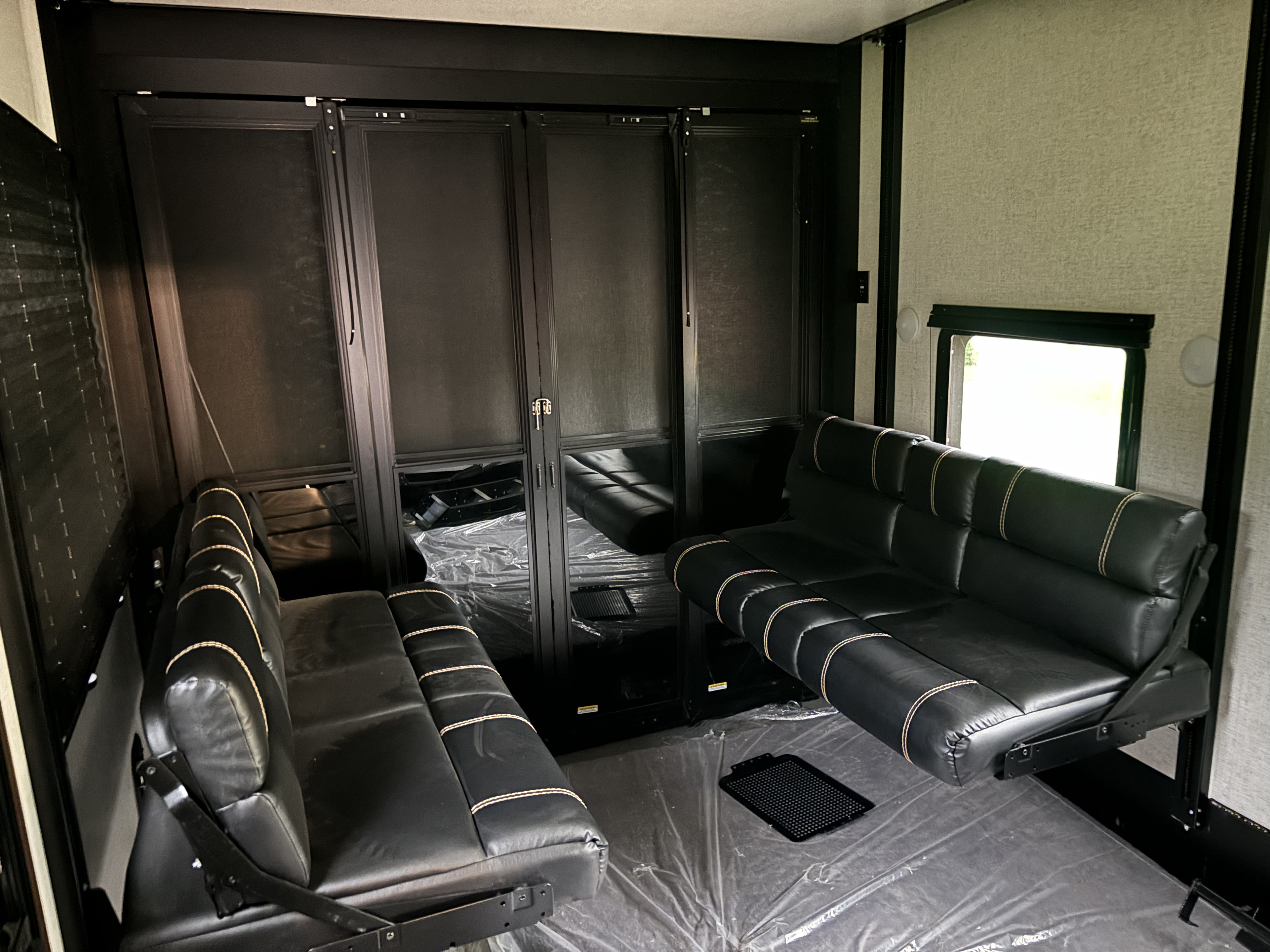 Inside an RV rental toy hauler, featuring elevated black leather sofas with beige stitching. Floor protected.. Dutchmen Voltage 2022