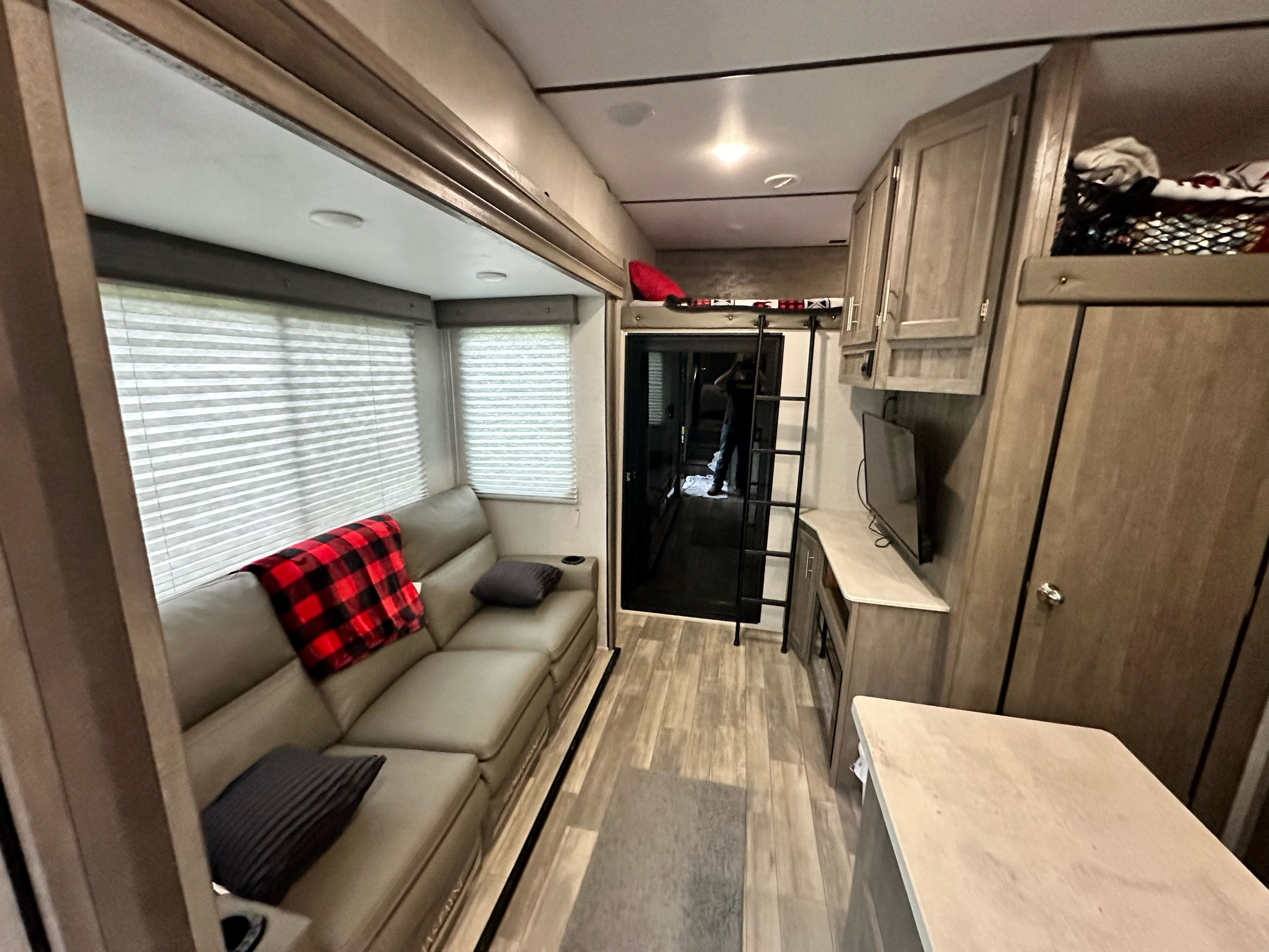 RV rental interior: well-appointed living area with a grey couch, plaid blanket, large windows, TV, and an elevated bunk bed.. Forest River Xlr Thunrderbolt 2021