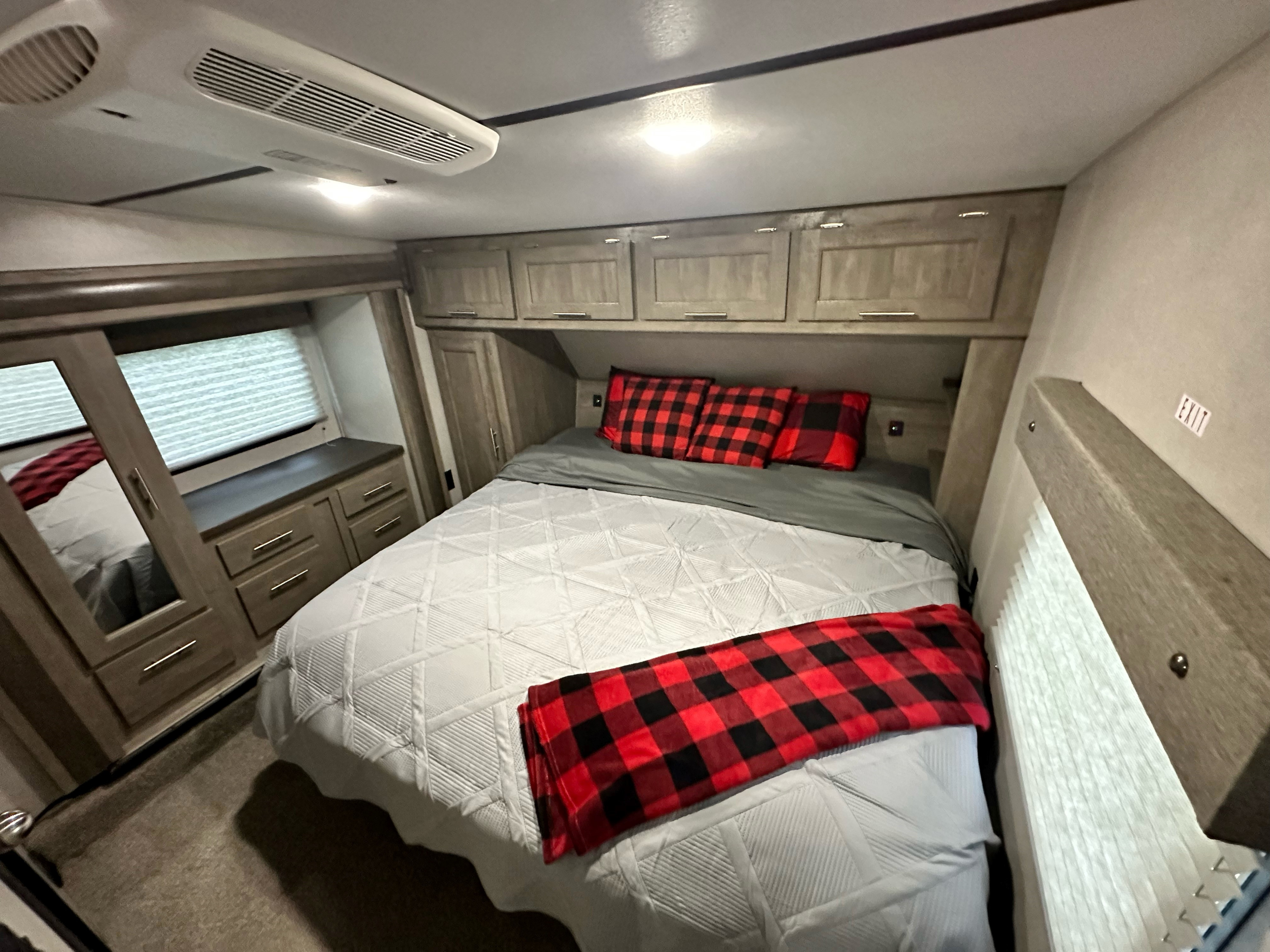 Cozy RV rental bedroom featuring a comfy bed with red plaid decor, overhead cabinets, and an AC unit.. Forest River Xlr Thunrderbolt 2021