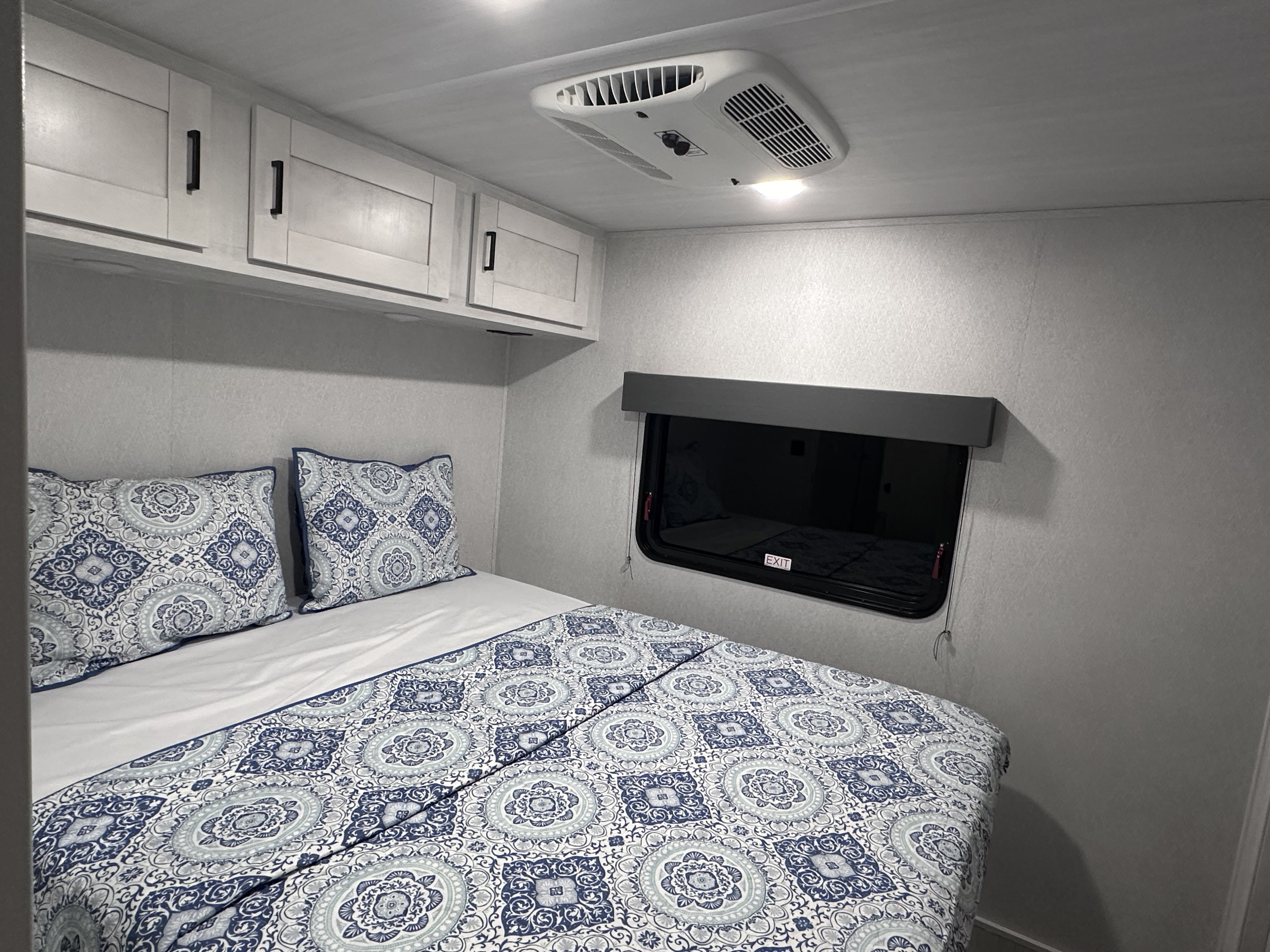 Comfortable RV rental bedroom with light gray walls, white cabinets, and blue patterned bedding.. EastWest Entrada 2024