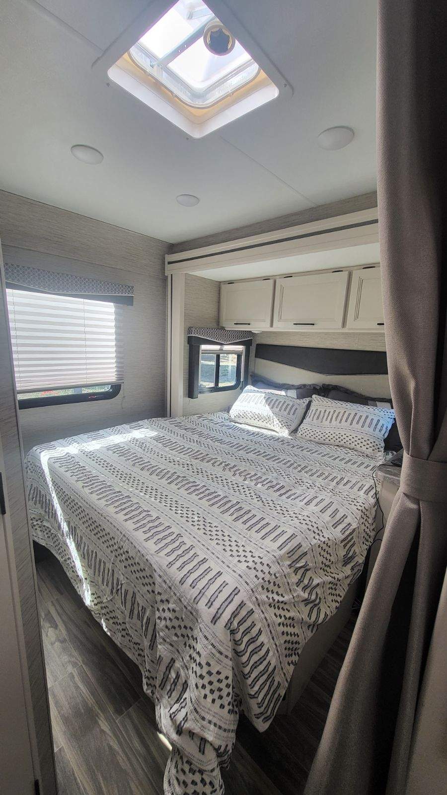 Cozy RV rental bedroom with a large bed, modern bedding, ample storage, and a bright skylight above.. Thor Four Winds 2023