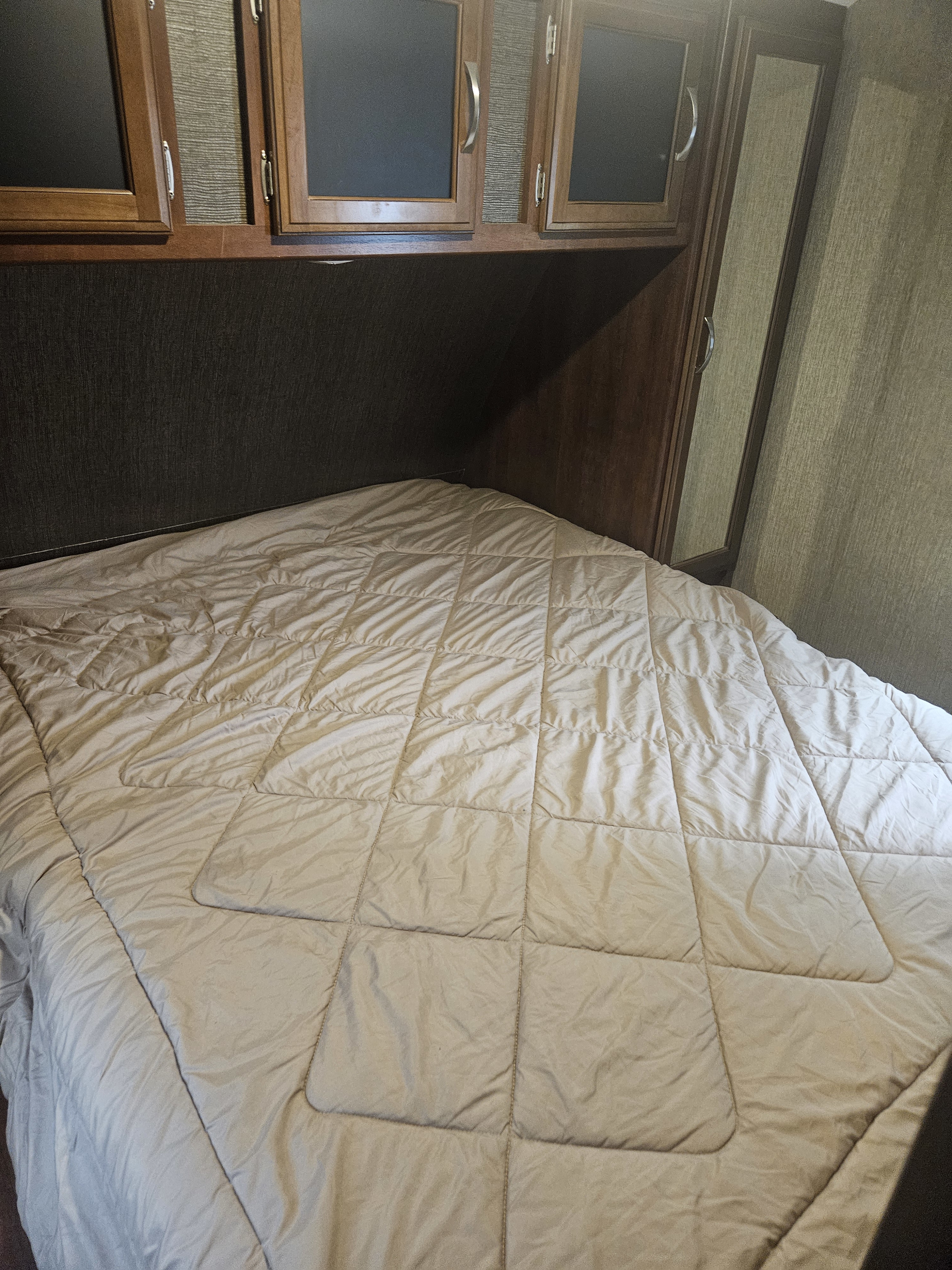 RV rental bedroom featuring a cozy bed, overhead storage cabinets, and a mirror, offering comfortable accommodations.. Keystone RV Passport Grand Touring 2018