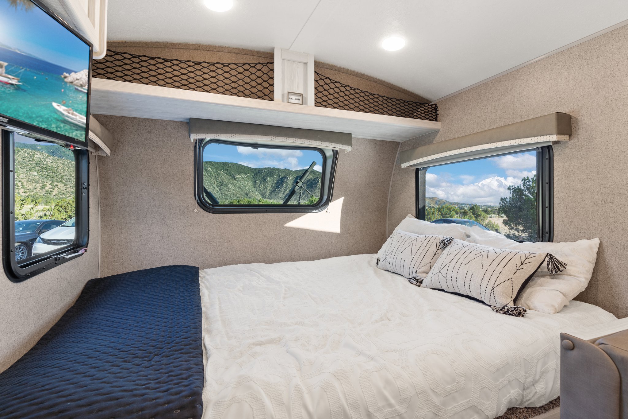 Experience comfort in this RV rental bedroom: cozy bed, mountain views from windows, TV, and storage for your travel needs.. Rockwood G19QB 2021