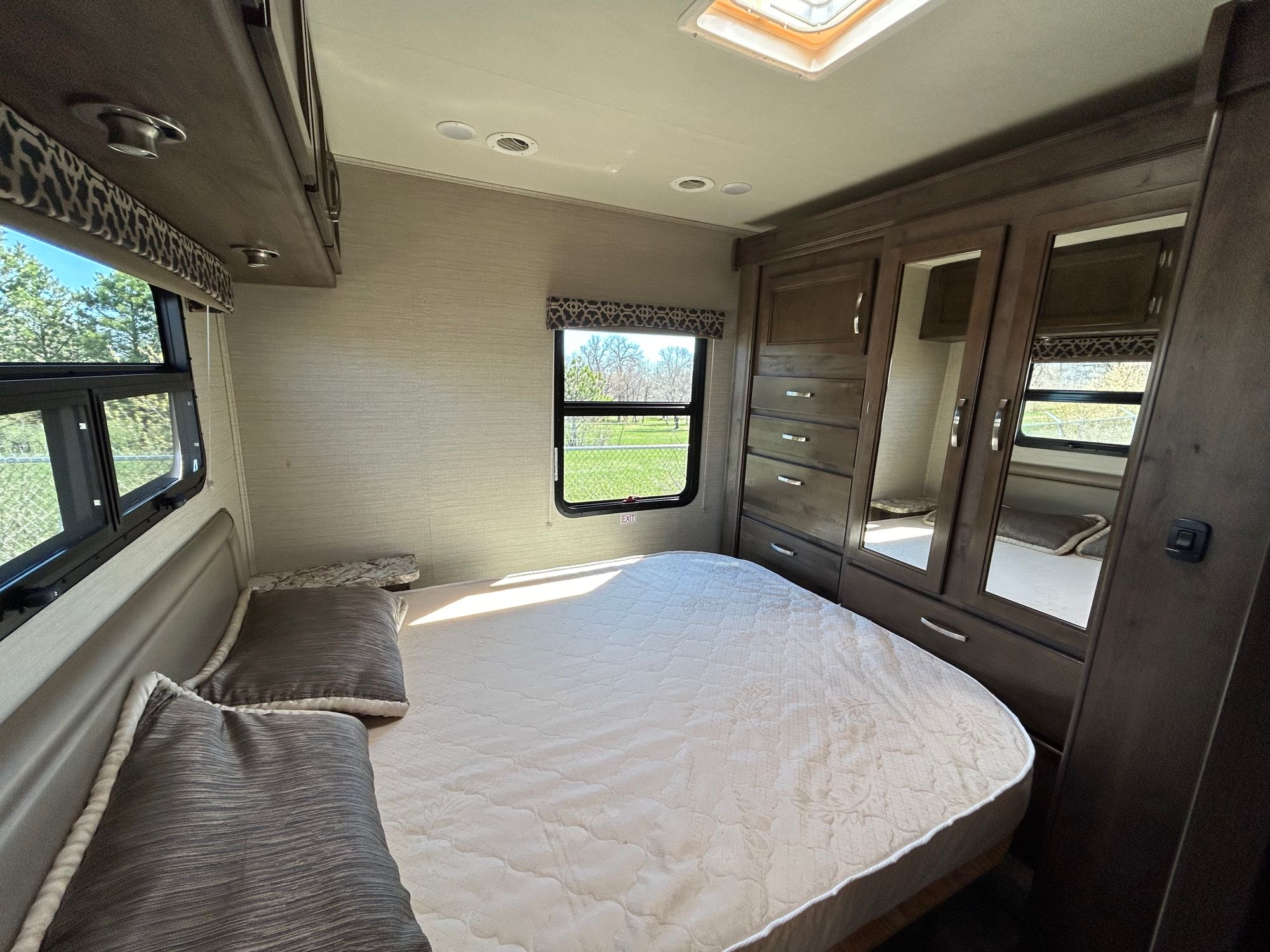 RV rental bedroom with a quilted bed, clear windows looking outside, and mirrored storage.. Redhawk 31F MC 2019