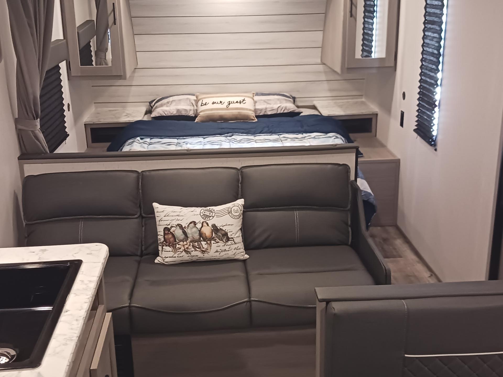 Cozy RV rental interior: bed, sofa with bird pillow, and kitchen. Ready for your adventure!. Coleman Lantern LT 274BH 2024