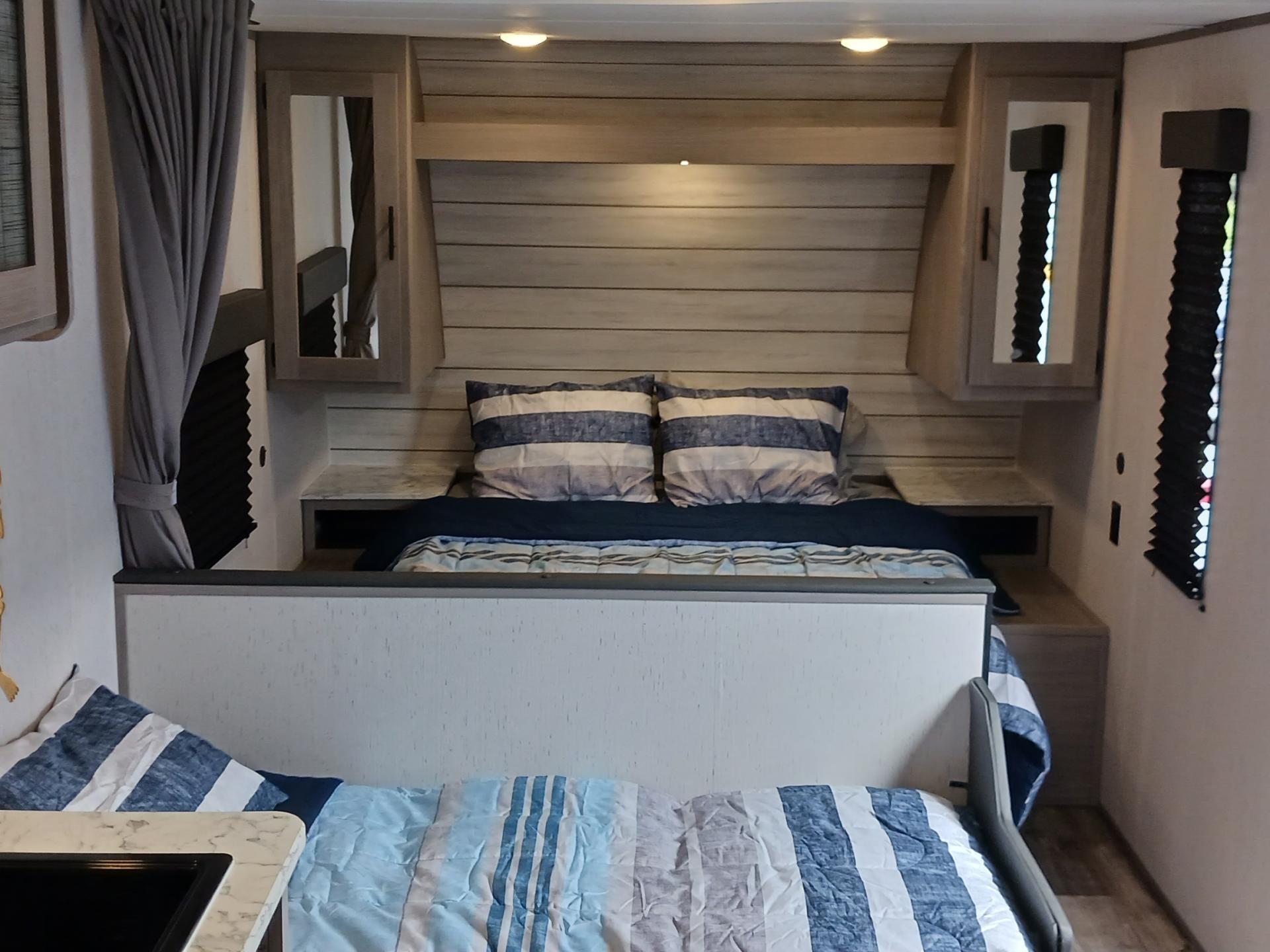 Inside an RV rental: a comfortable bedroom with striped bedding, bunk, overhead cabinets, and soft lighting.. Coleman Lantern LT 274BH 2024