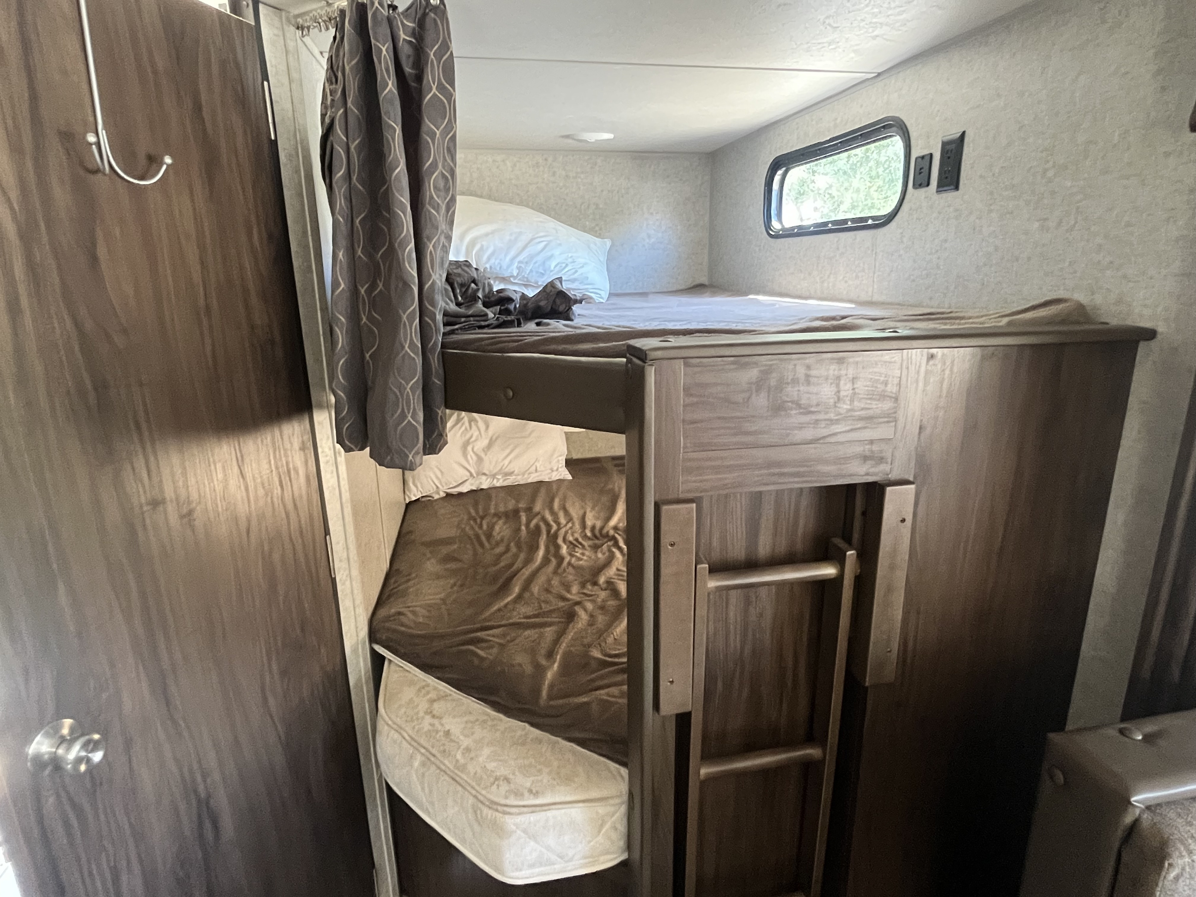 A clear view inside an RV rental, showcasing compact bunk beds. This cozy sleeping area includes mattresses, a window, and a privacy curtain.. Forest River Cherokee Grey Wolf 2019