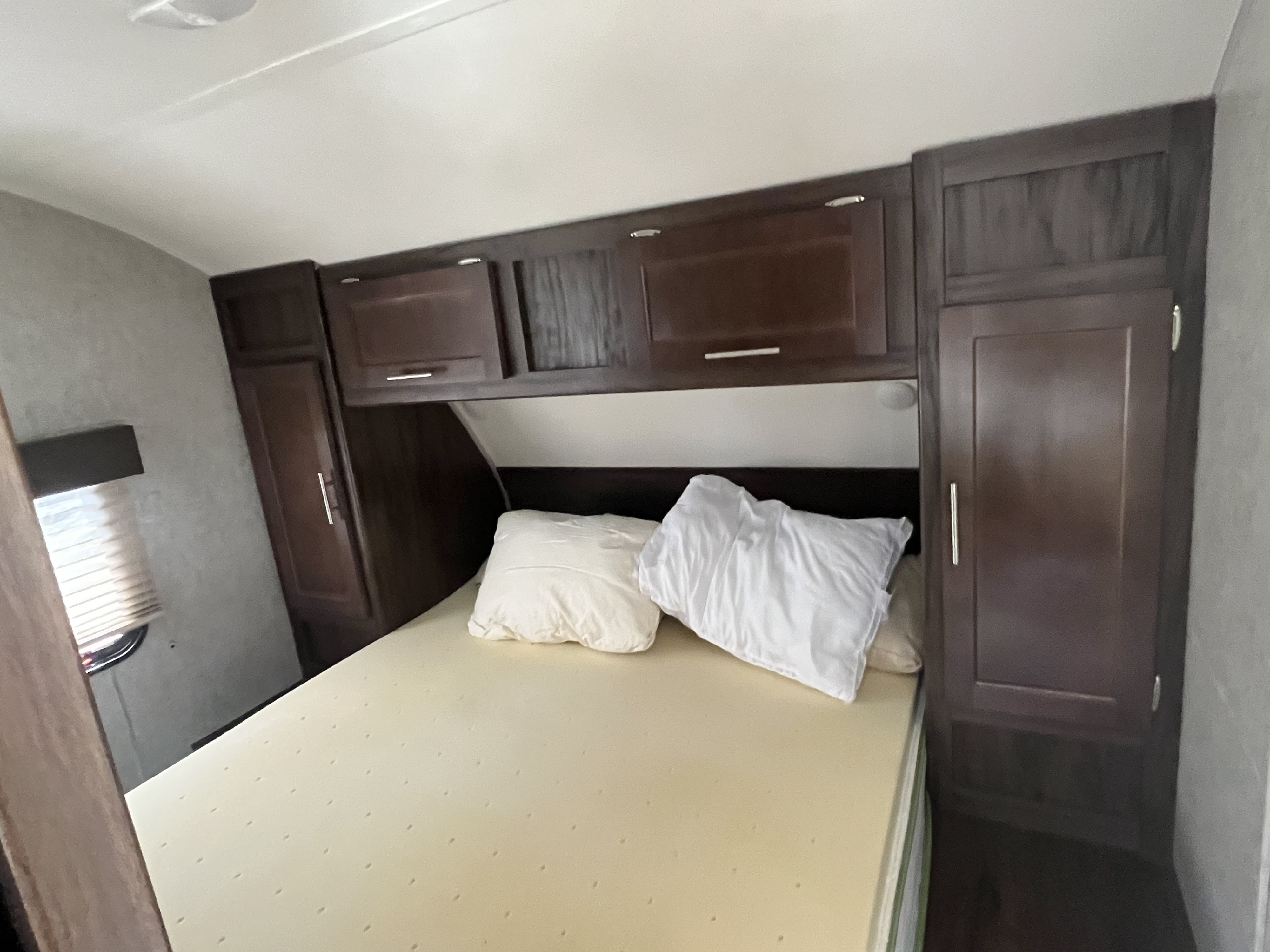 RV rental bedroom: Features a bed with foam mattress, dark wood storage cabinets, and a window with blinds.. Forest River Cherokee Grey Wolf 2019