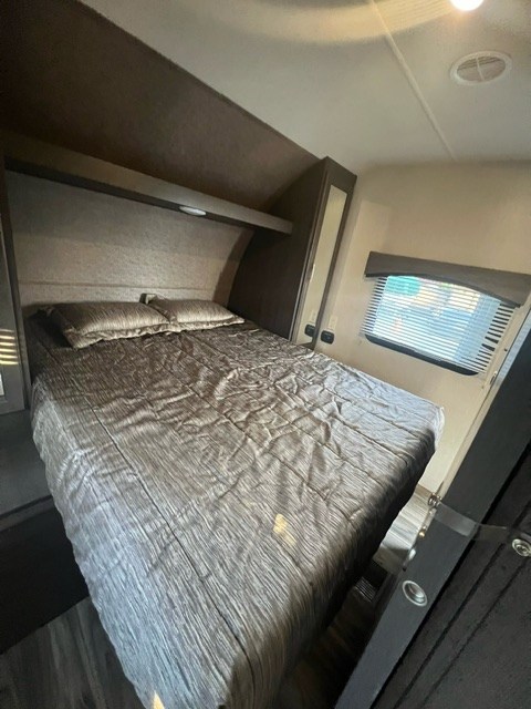 Cozy RV rental bedroom featuring a comfortable bed, overhead storage, and window blinds. Ideal for travel comfort.. Forest River Evo 2017