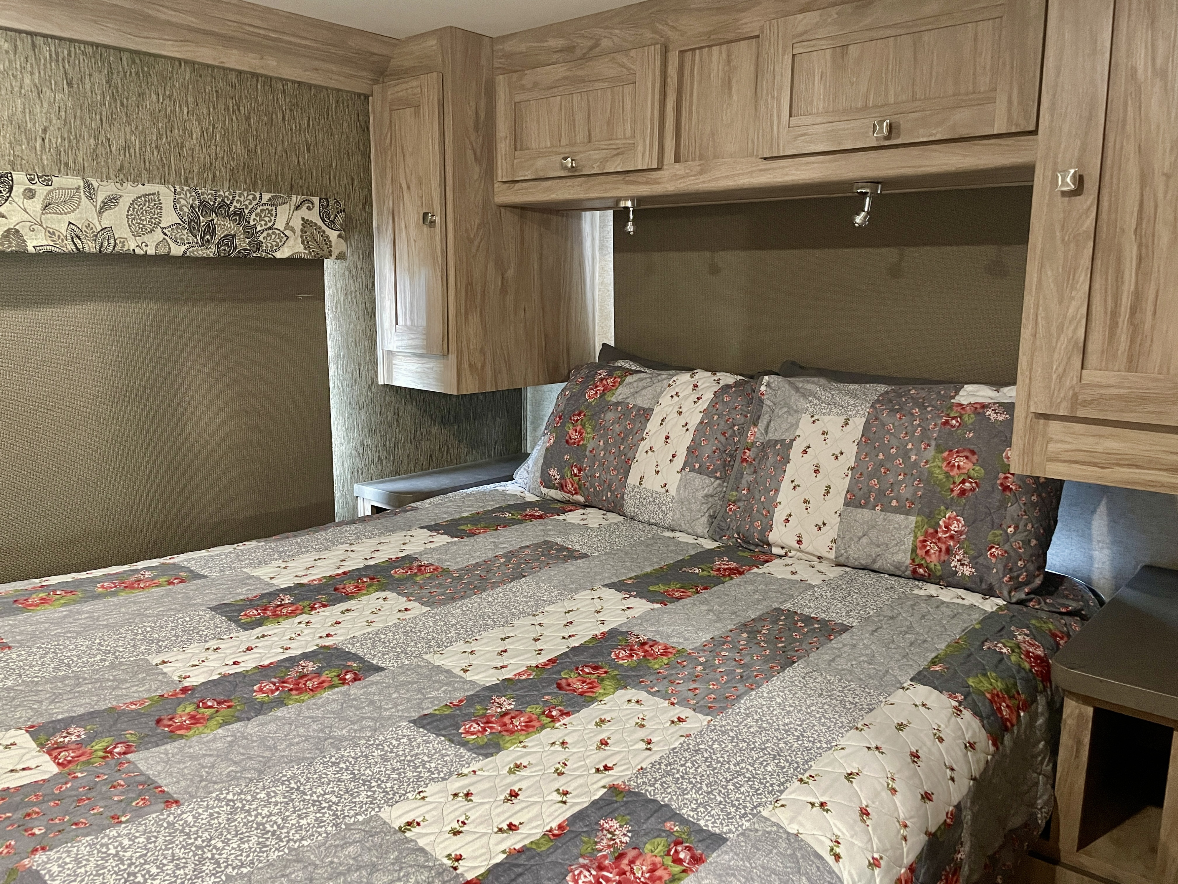 Cozy RV rental bedroom featuring a floral quilt, wood cabinetry, and reading lights for comfortable travel.. Forest River Forester 2017