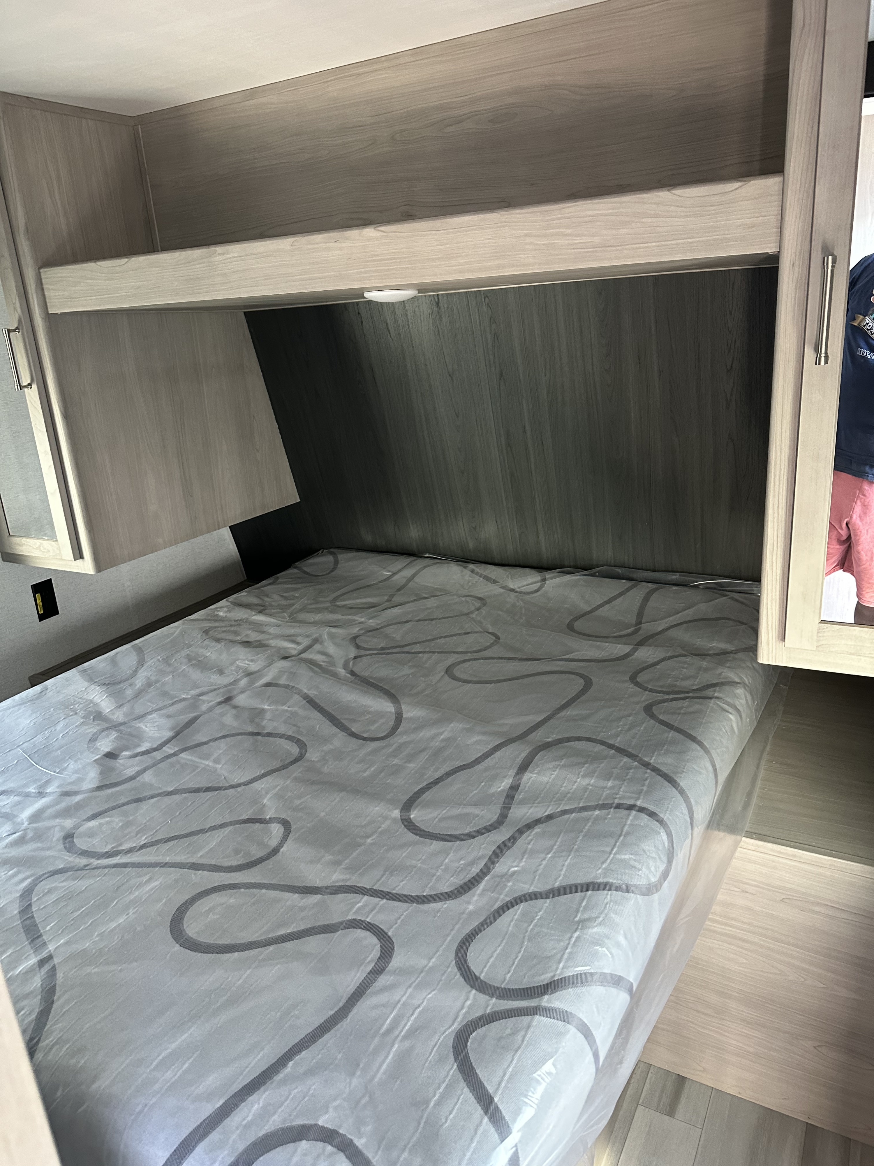 Clean RV rental bedroom featuring a new bed, overhead storage, and modern wood finishes. Ready for your next adventure.. Keystone RV SG261BHC 2024