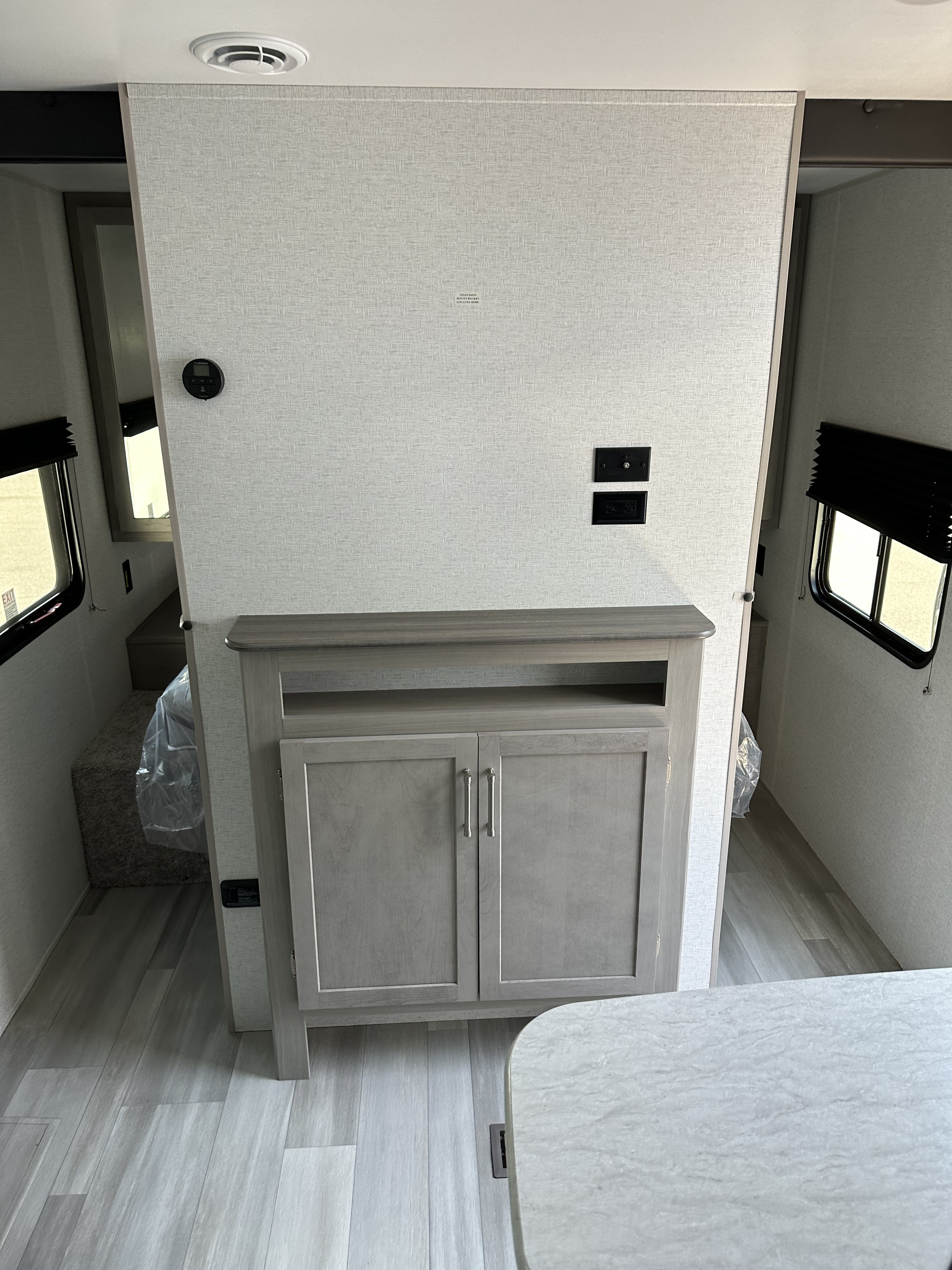 Inside an RV rental, a divider wall with TV hookups and built-in light wood cabinetry separates living and bedroom areas.. Keystone RV SG261BHC 2024
