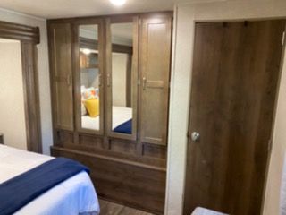 RV rental bedroom: large wooden wardrobe with mirrored doors, comfortable bed, and wood door on right. Ideal for travel.. Forest River Palomino Puma 2020