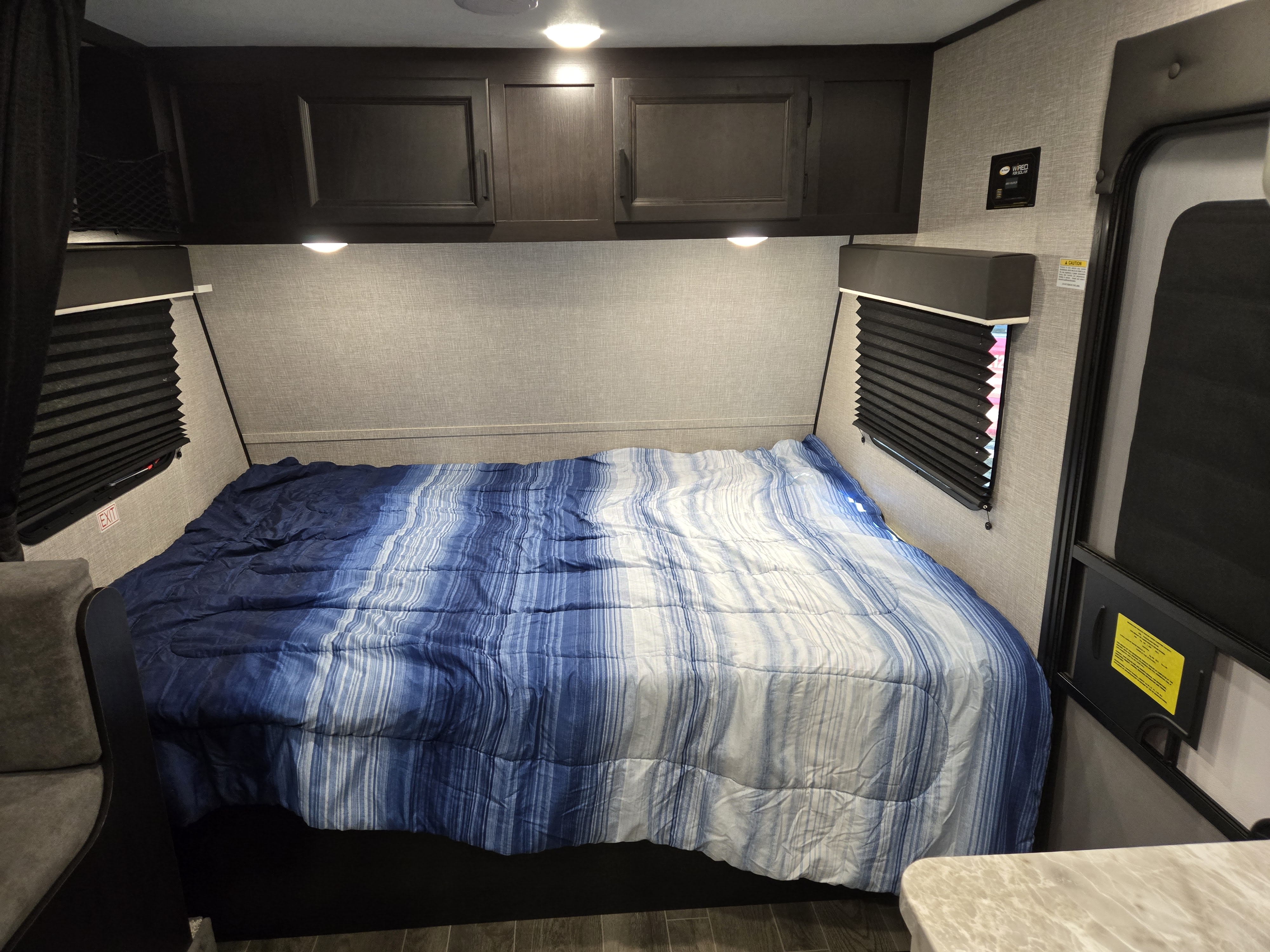 Inside this RV rental: A comfortable sleeping area with blue striped bedding, overhead cabinets, and window blinds.. Jayco Jay Flight SLX 2022