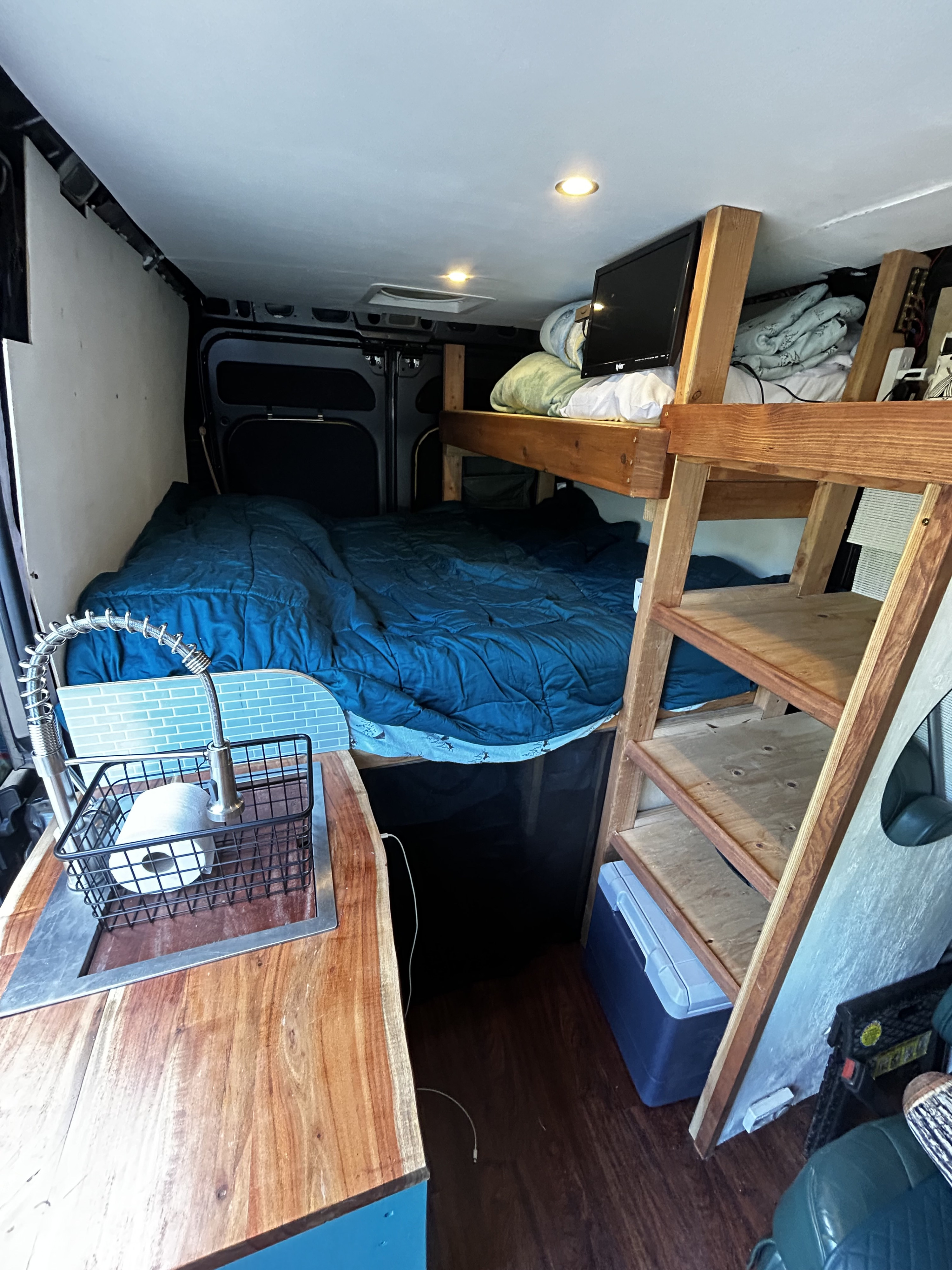 Explore this RV rental's clever interior: a cozy bed, kitchen sink, and overhead bunk for compact living on the go.. Dodge Ram 1500 2017