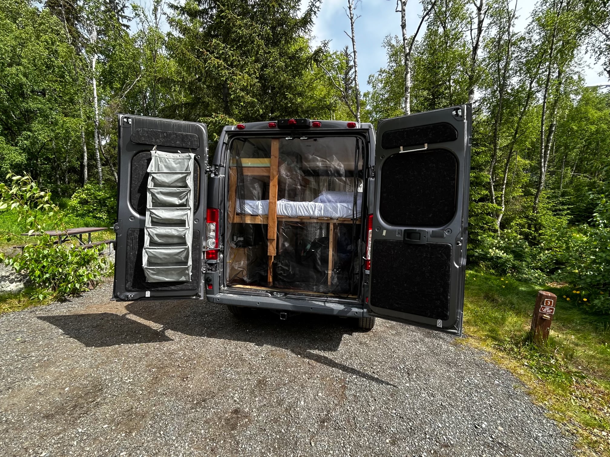 Explore this RV rental camper van with open rear doors revealing bunk beds, parked at a scenic campsite.. Dodge Ram 1500 2017