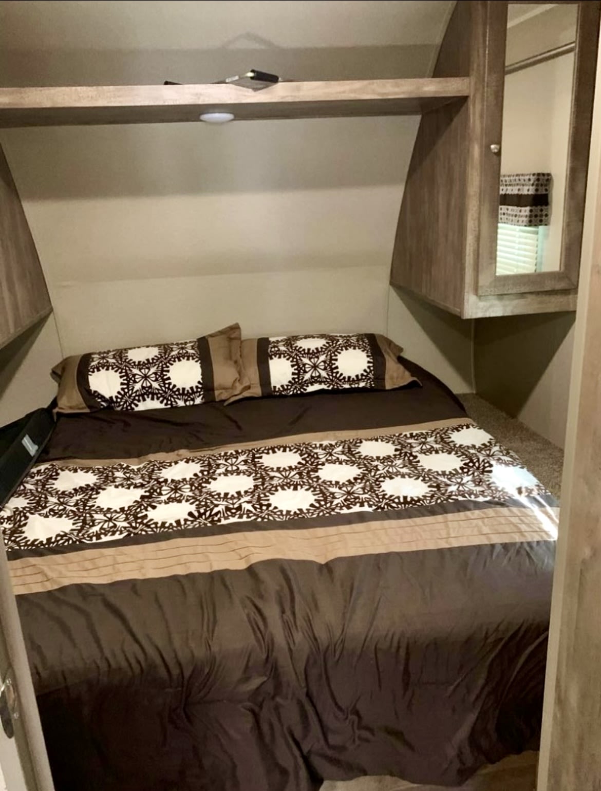 Cozy RV rental bedroom with patterned brown and beige bedding, overhead storage, and mirrored cabinet.. Palomino Puma 2017