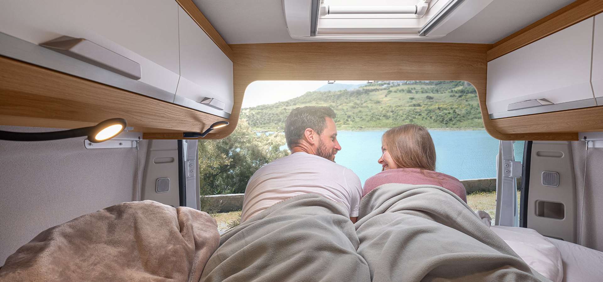 Couple enjoys a scenic lake view from their cozy RV rental bed, perfect for nature getaways.. Knaus BOXLIFE 540 2024