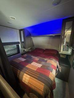 Experience comfort in this RV rental's cozy bedroom. Features a large bed, blue accent lighting, and storage for your travel needs.. Jayco Jay Flight SLX 2020
