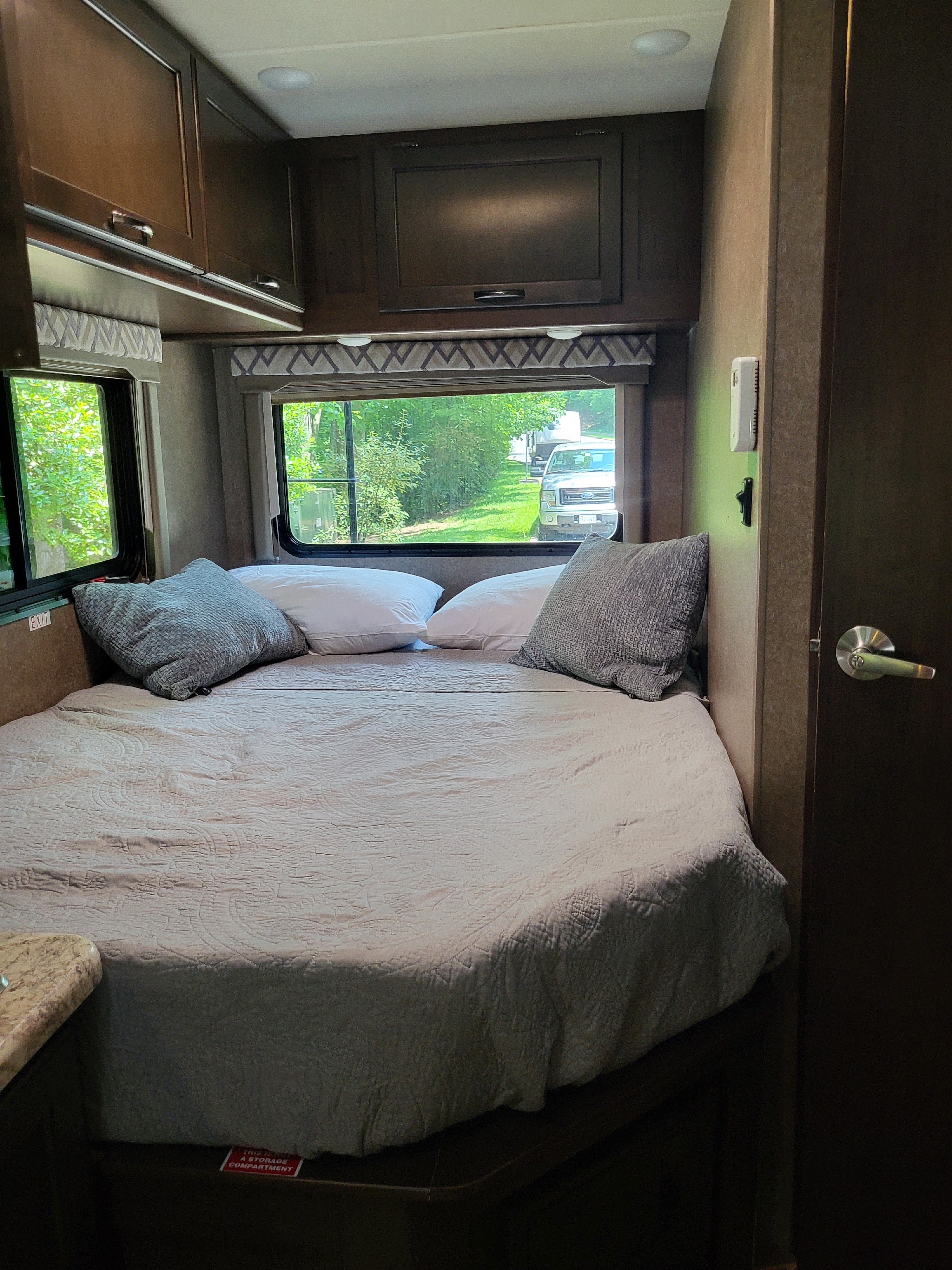 Cozy RV rental bedroom with a comfy bed, overhead cabinets, and bright windows offering a view of nature.. Thor Four Winds 2020