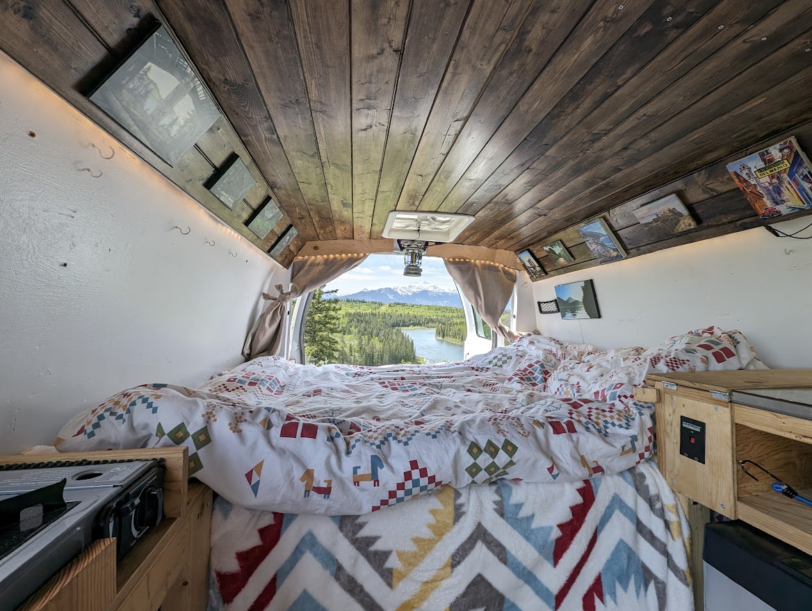 Inside an RV rental: a cozy van life bedroom with wood accents & a stunning lake/mountain view from the rear. Perfect mobile home.. Ford Econoline E250supercab 2012